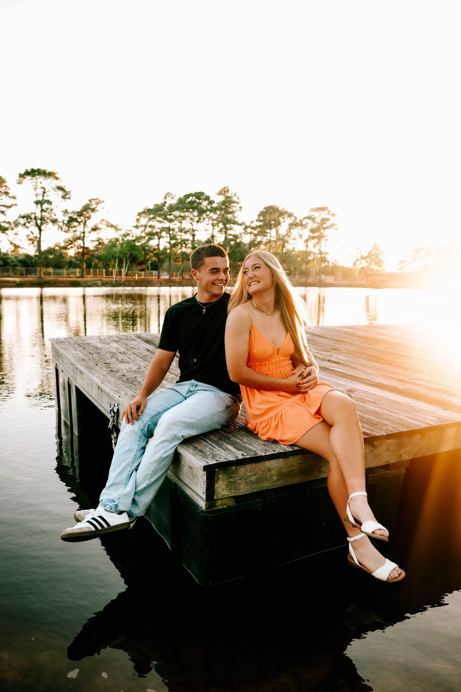 Couple sitting on wooden dock during sunset creating romantic silhouettes over water.