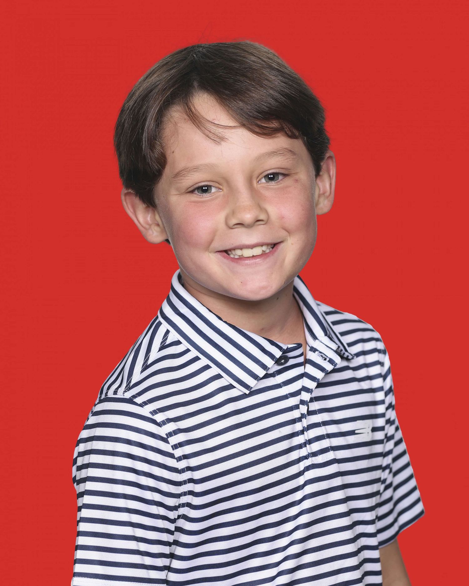Child in navy and white striped collared shirt poses against red background.