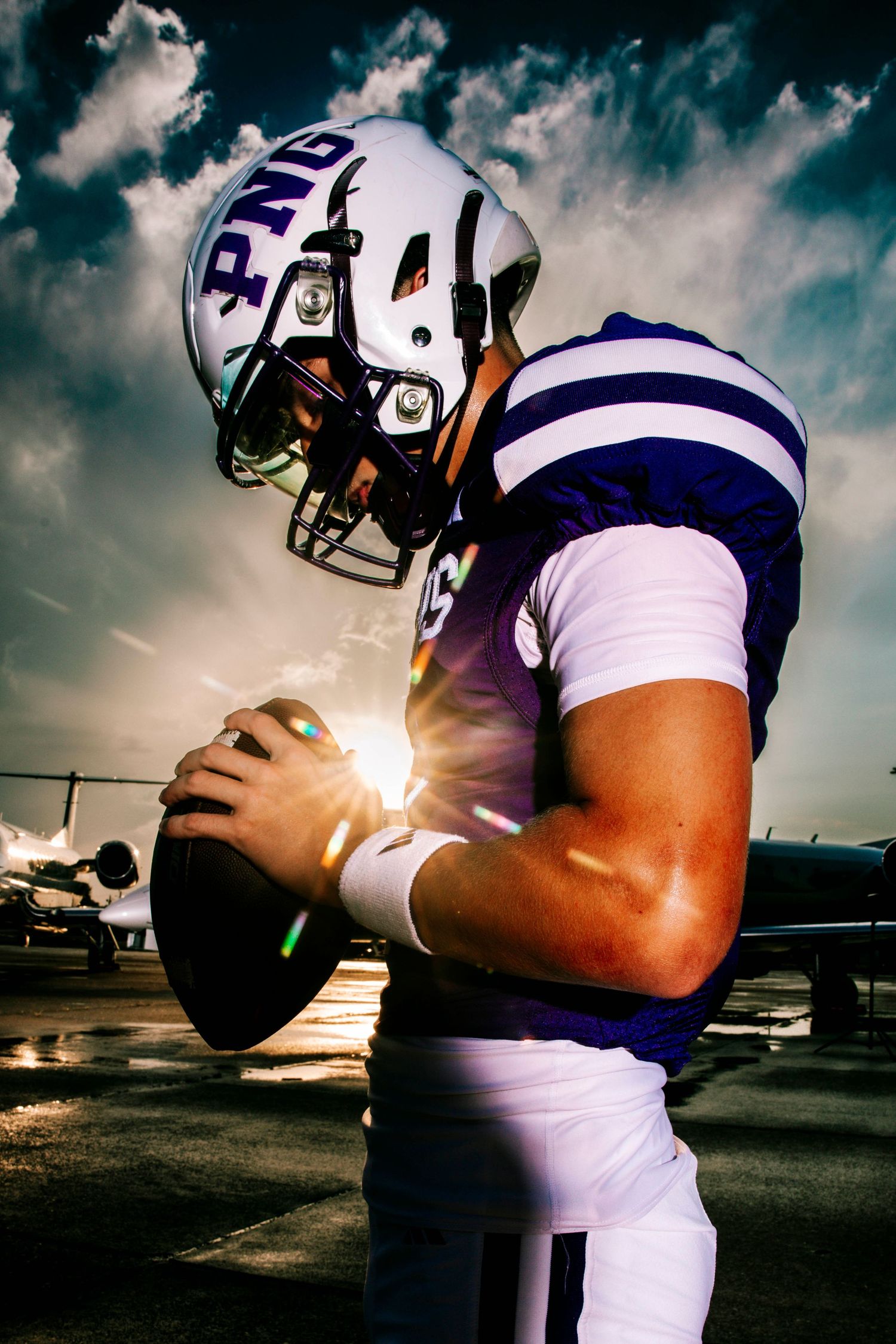 Football players in purple and white uniforms photographed against dramatic sky.