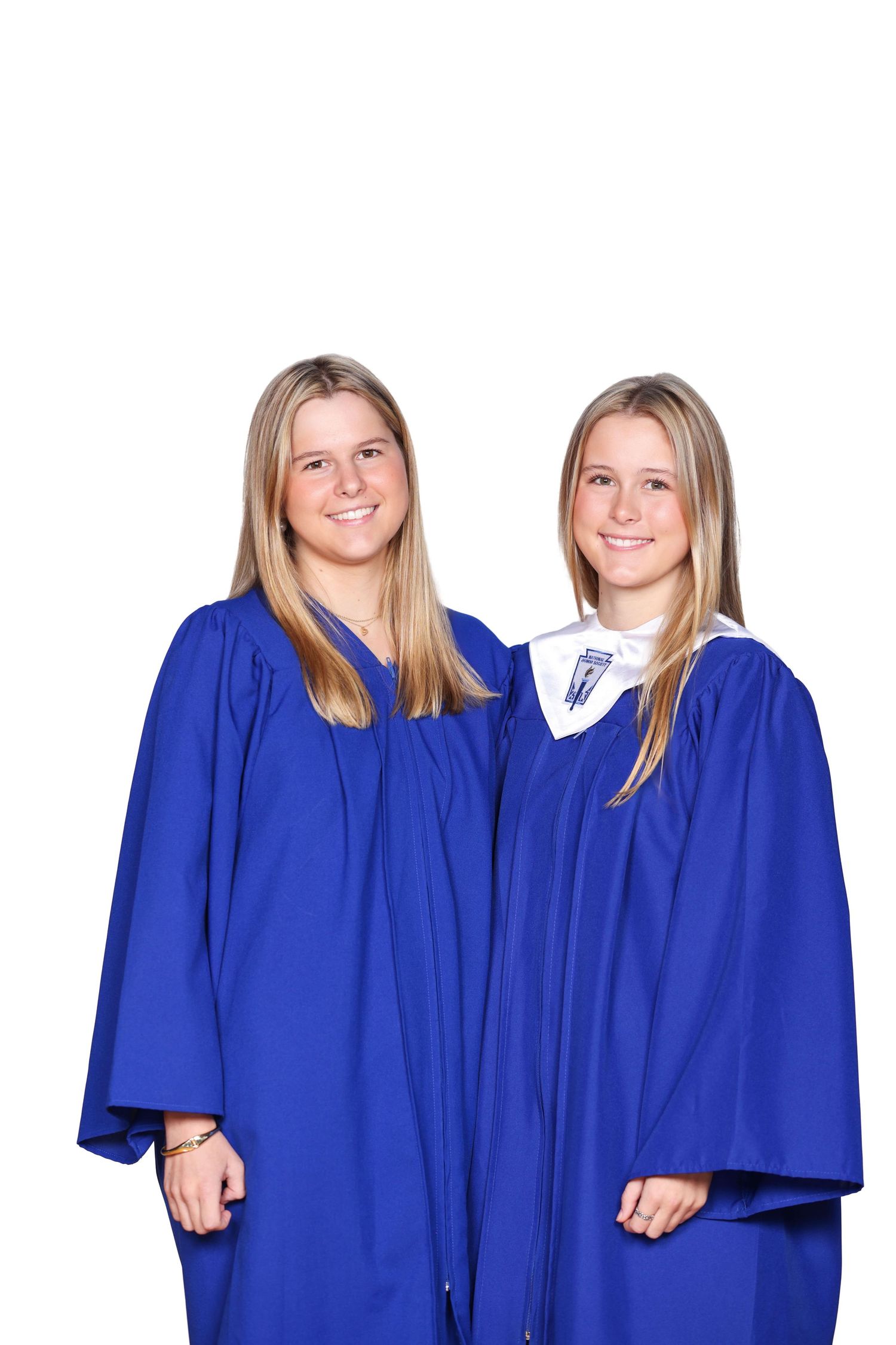 Two graduates wearing royal blue graduation gowns smile together for a portrait.