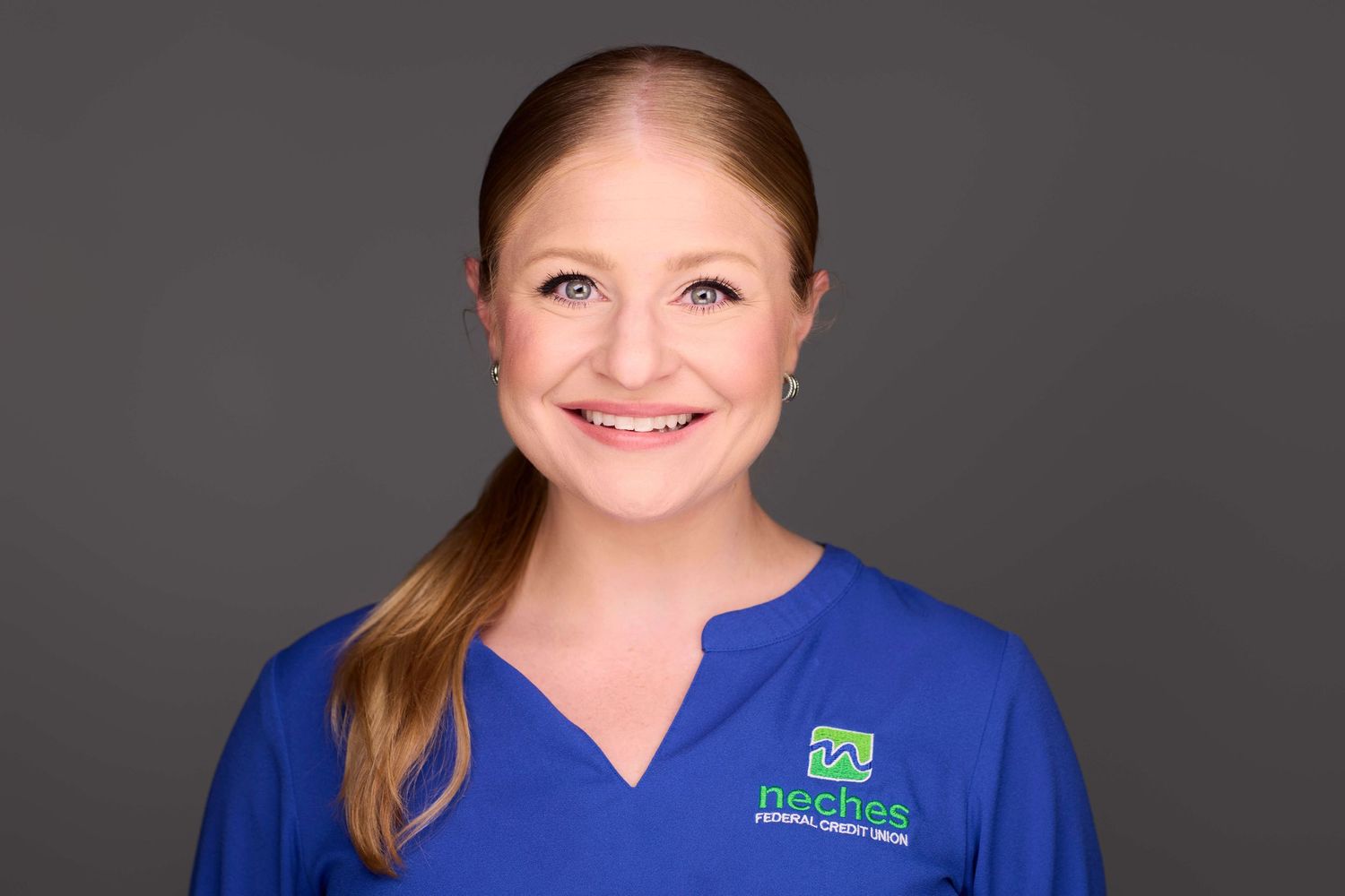 Professional headshot of person in blue medical scrubs against gray background.