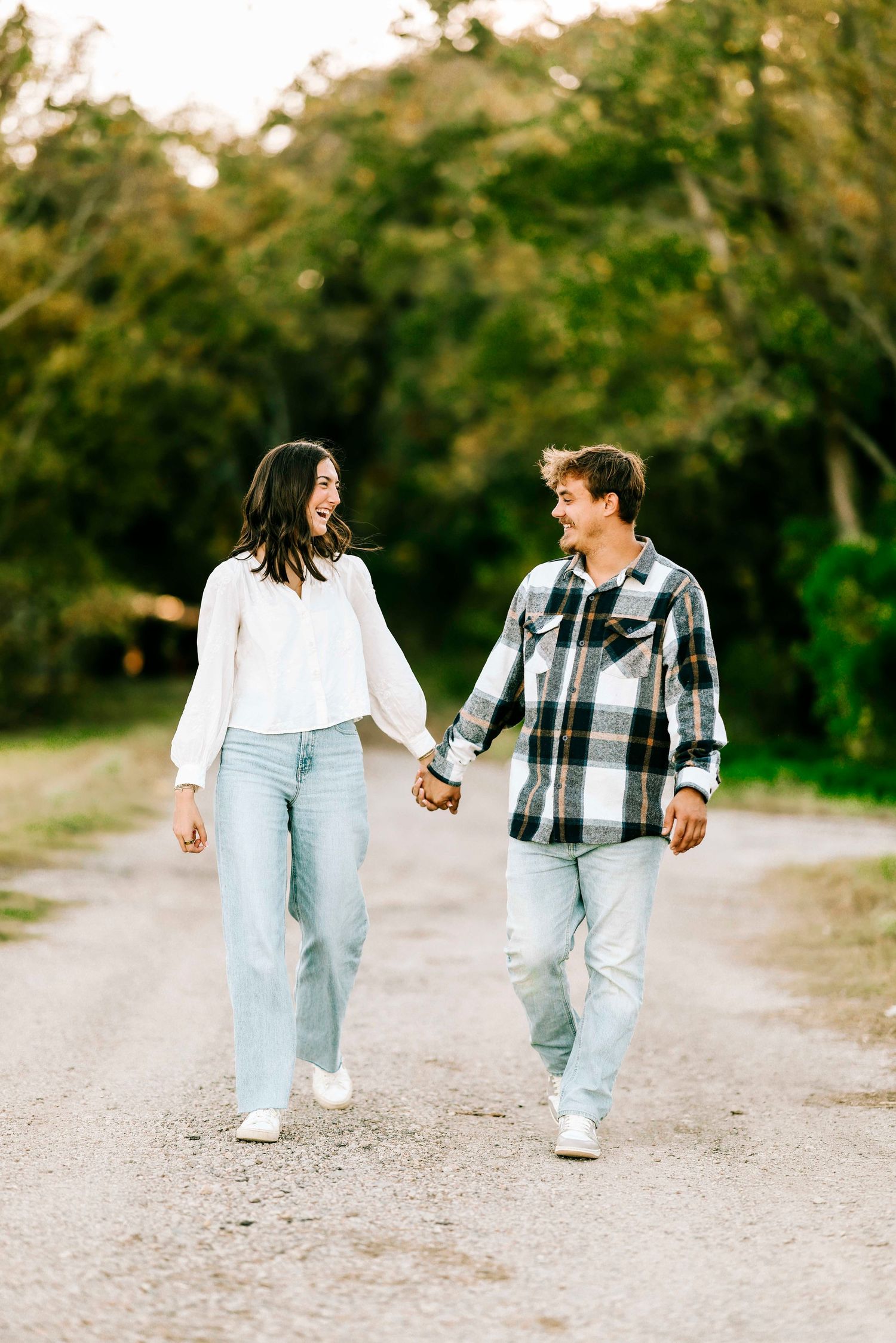 A couple holding hands while walking down a dirt path surrounded by lush greenery at sunset.