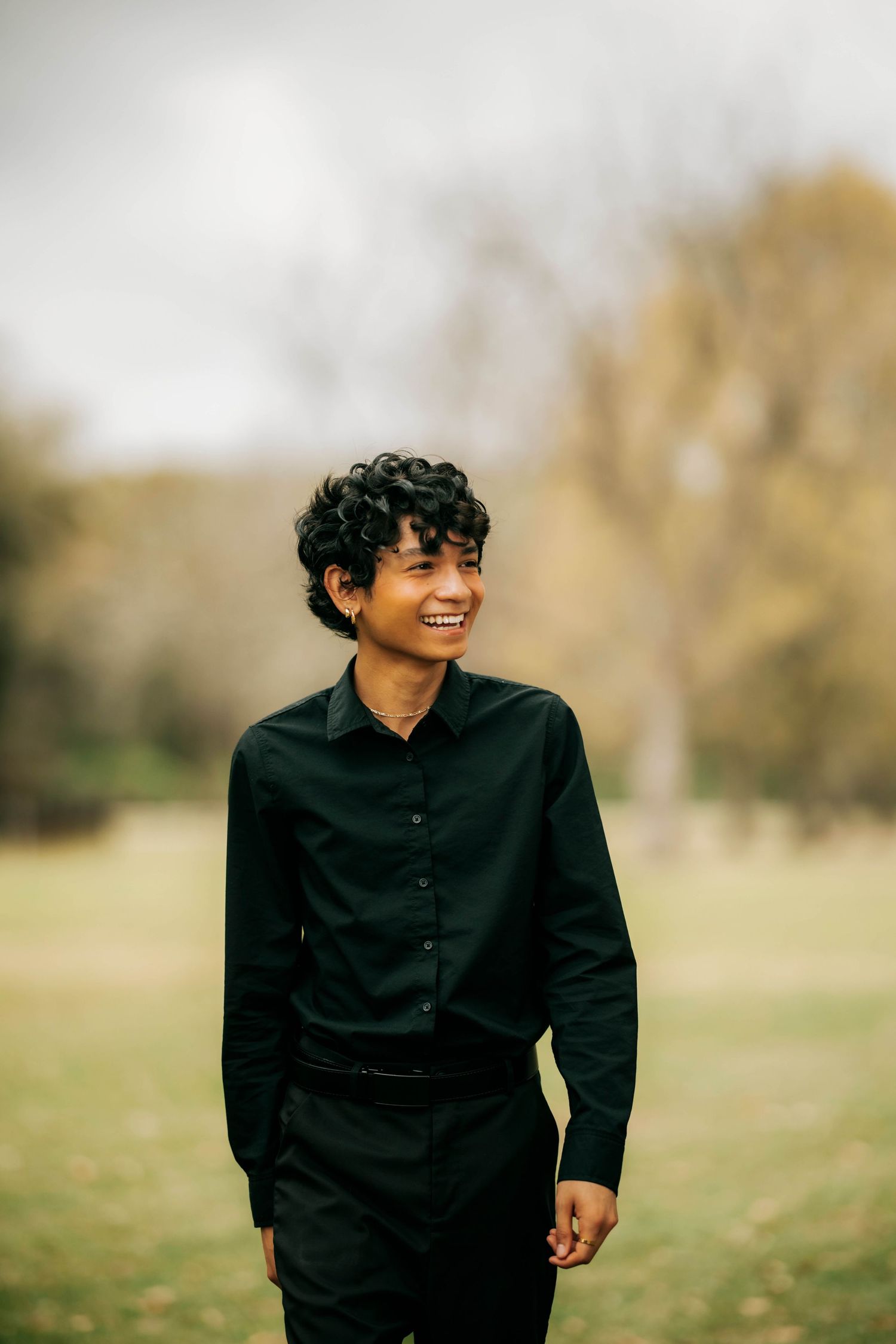 Person in black button-down shirt smiles while standing in outdoor setting during golden hour.