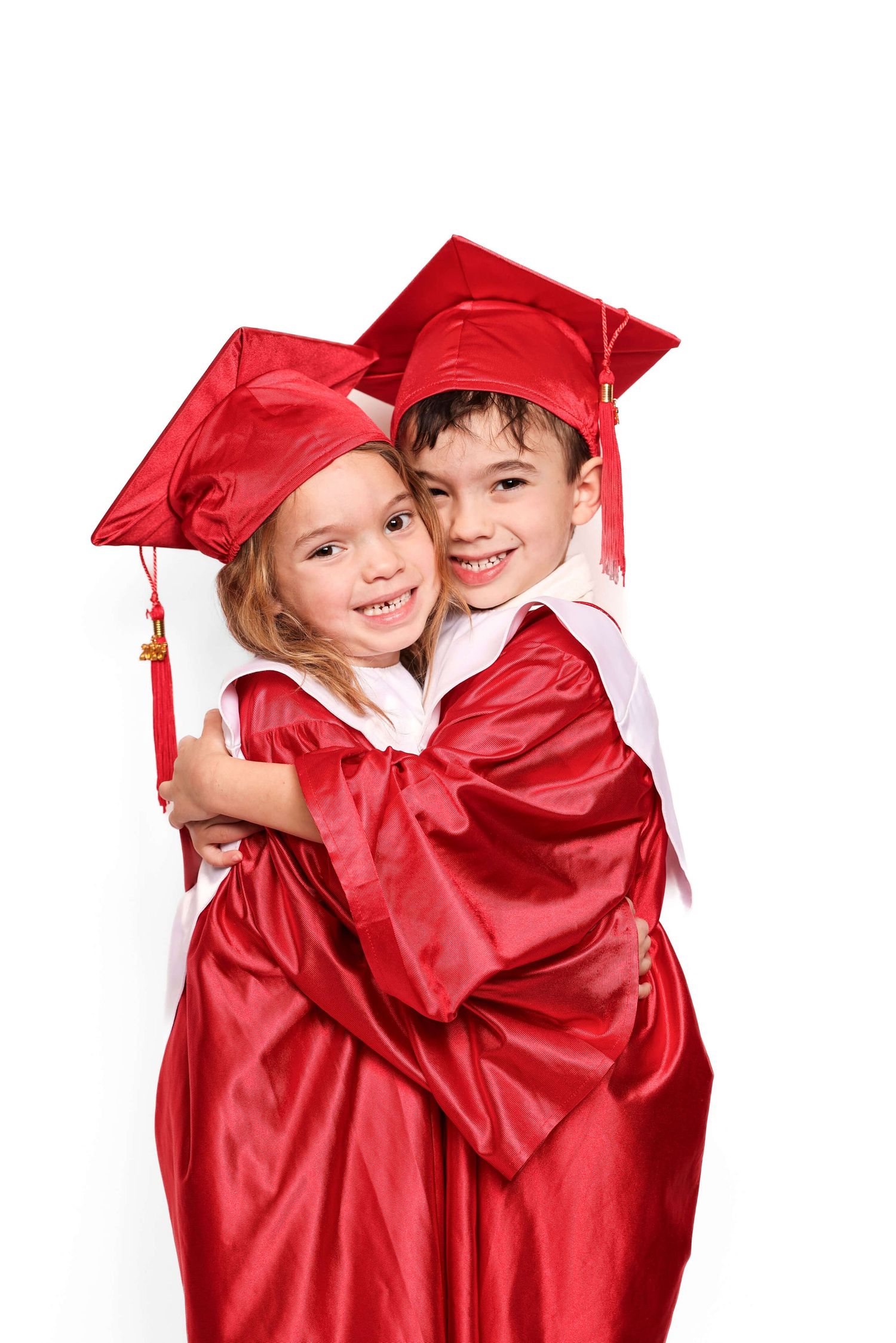 Children in bright red graduation gowns embrace during celebration ceremony.