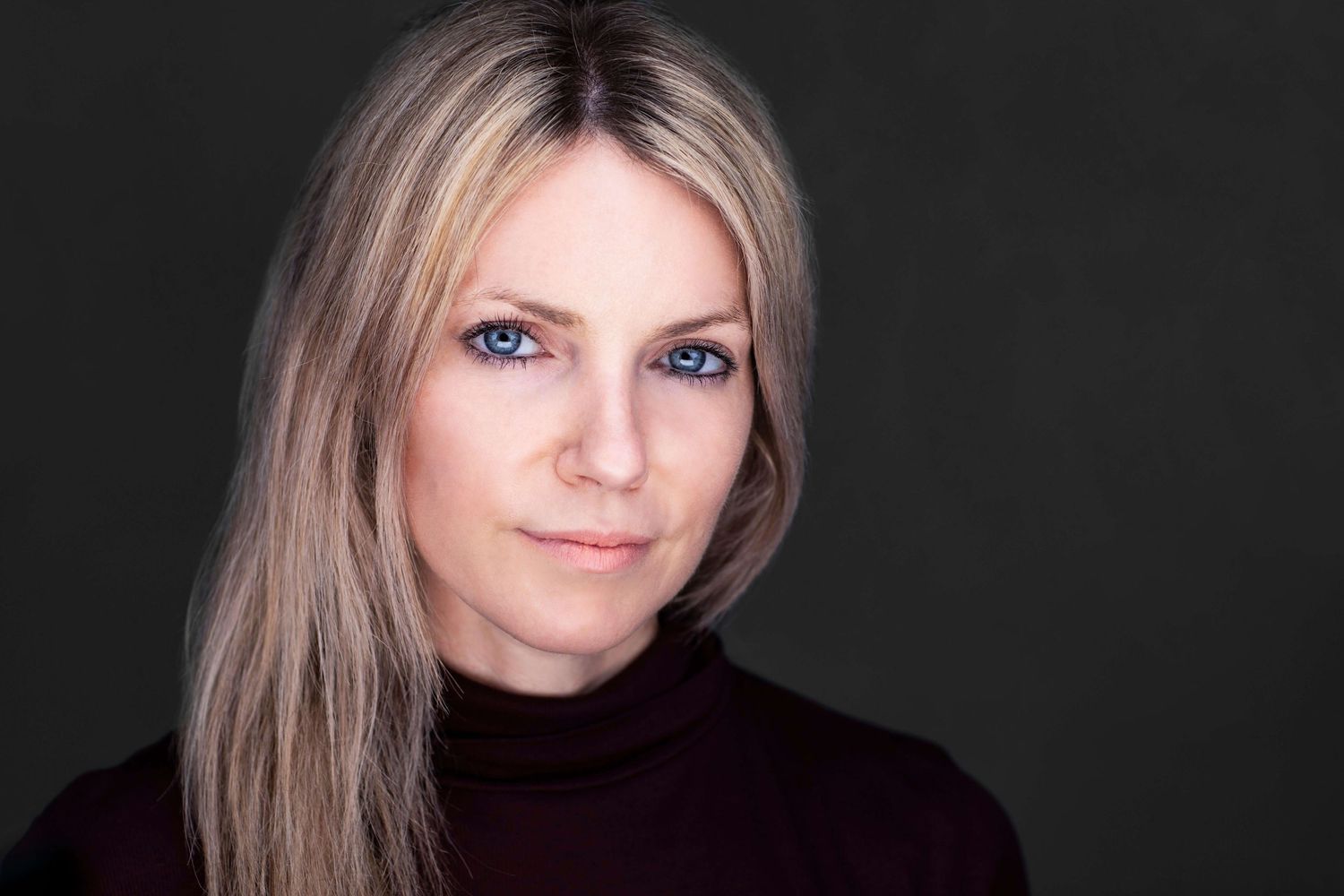 Professional headshot of person in dark top against black background.