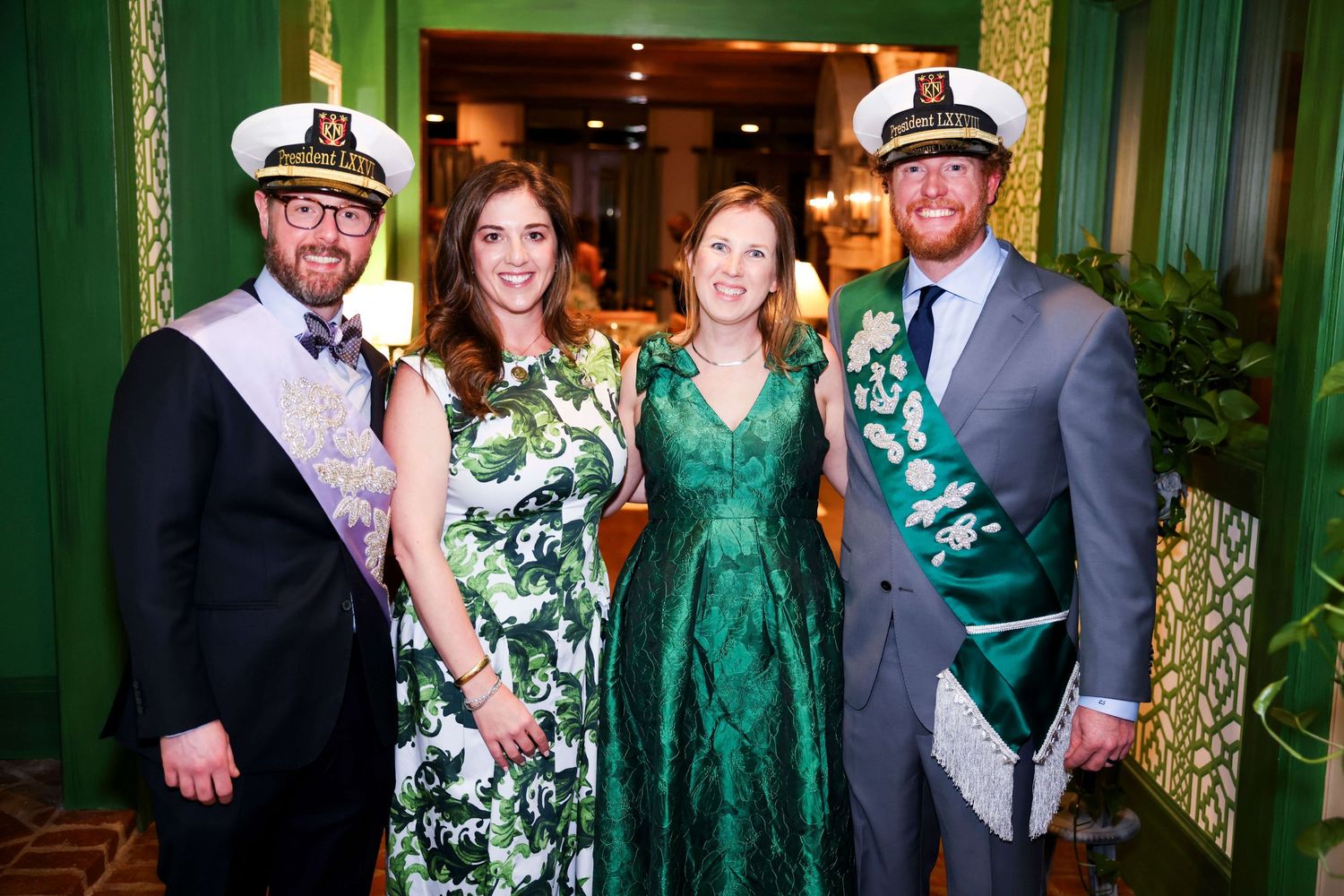 Four people dressed in formal attire including green dresses and sashes pose together at an elegant event.