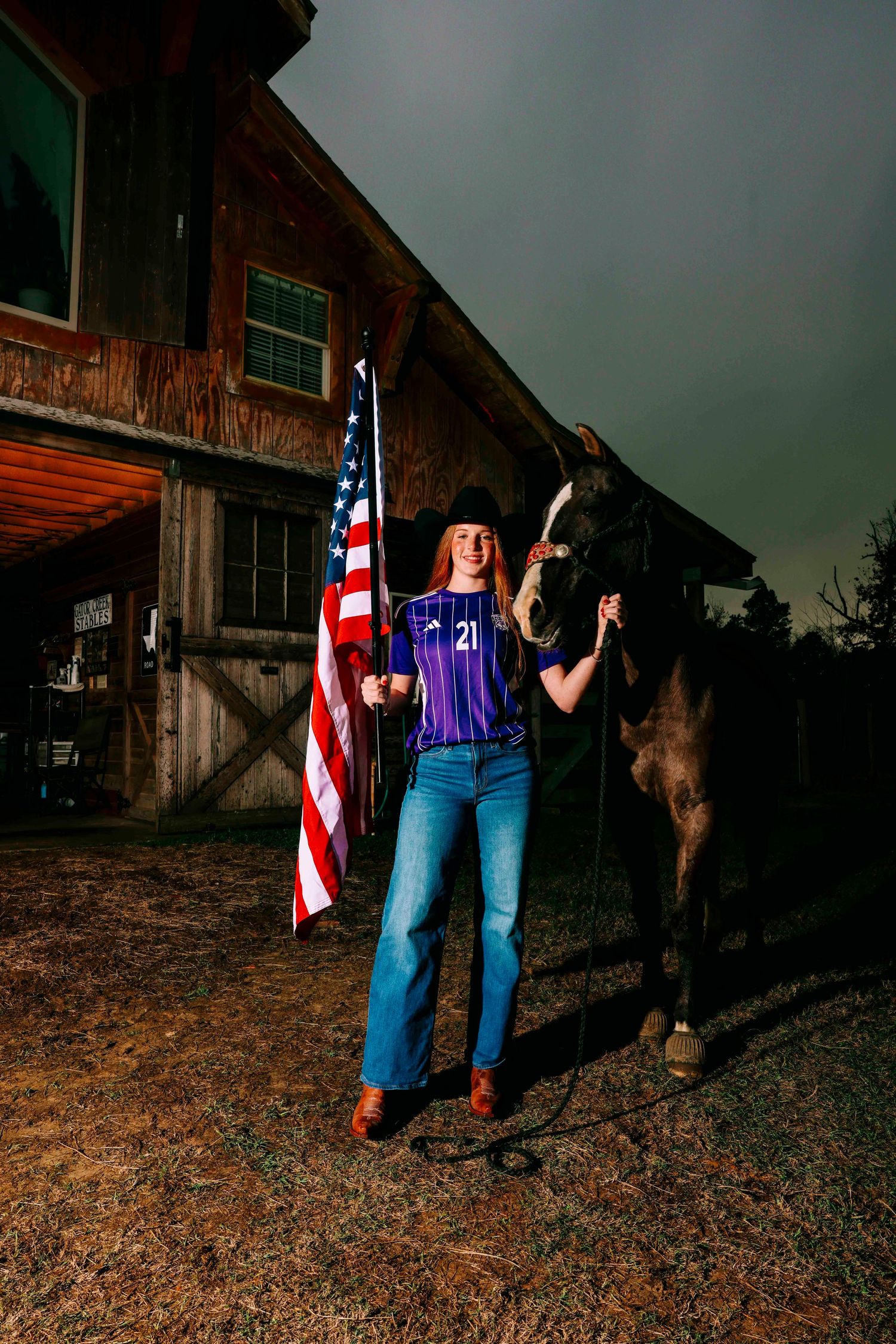 Patriotic scene with American flag and cowboy boots against rustic barn backdrop at dusk.