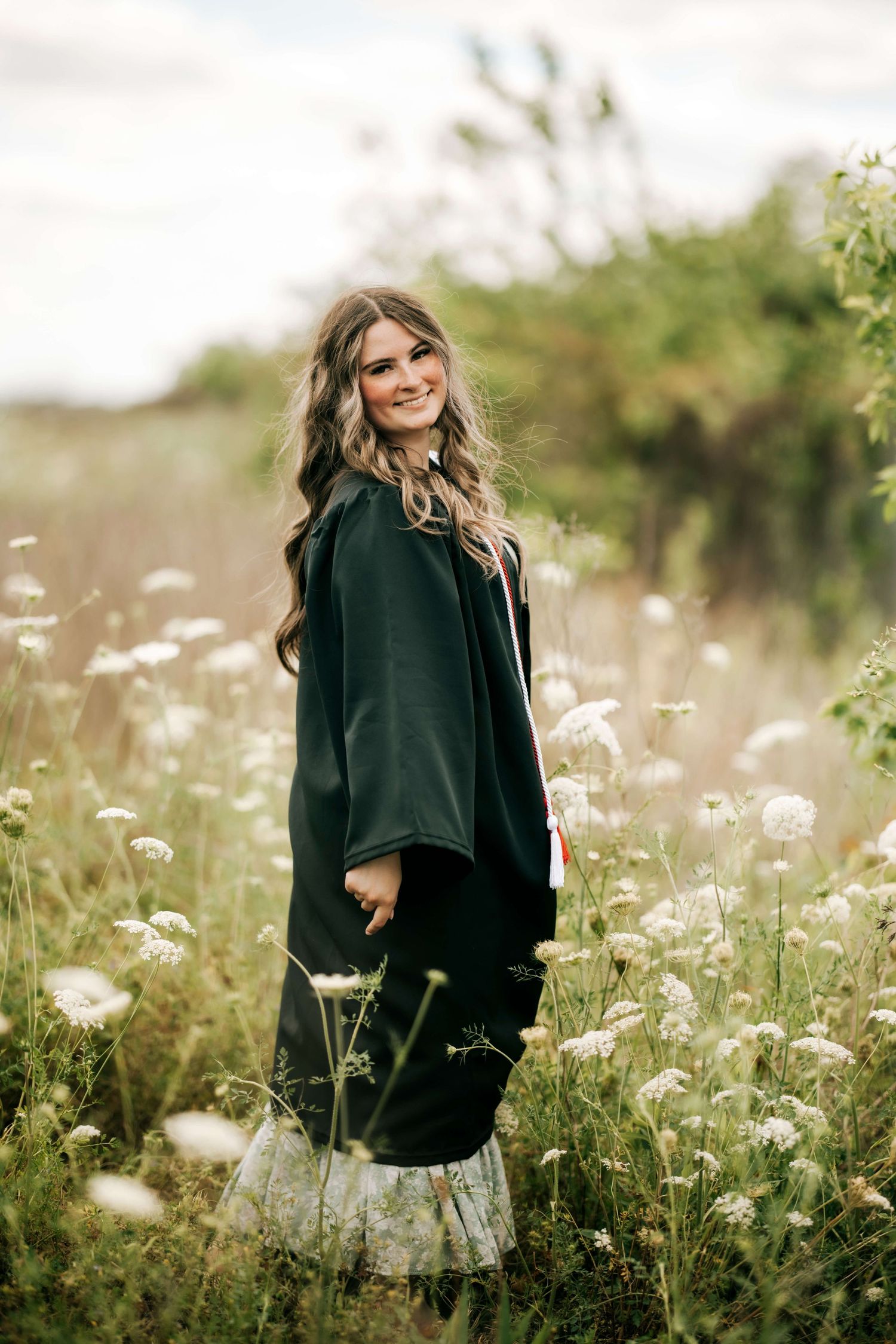 A person in a dark coat stands among wildflowers in a dreamy outdoor setting.