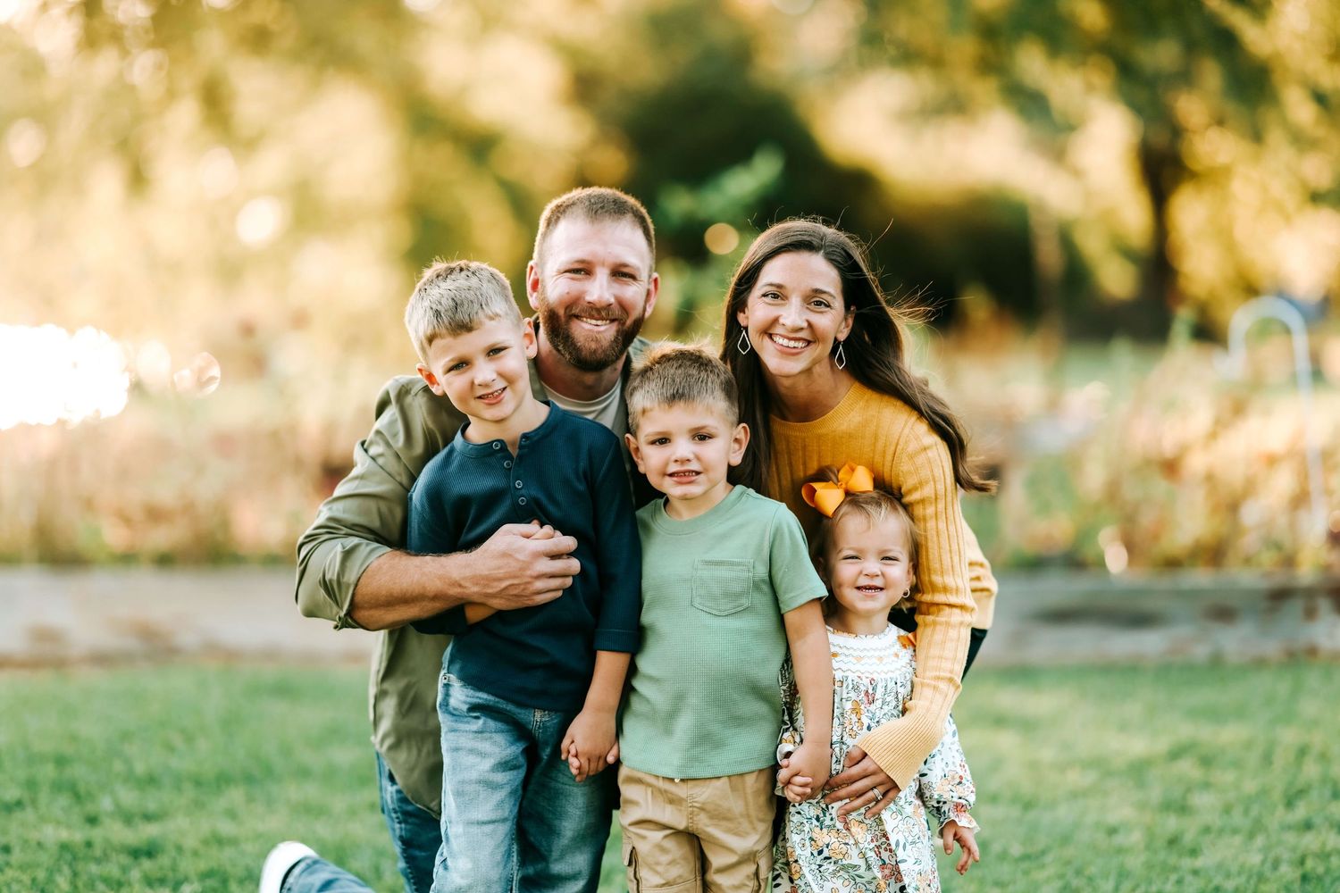 Family members embrace while posing for casual outdoor portraits in a park setting.