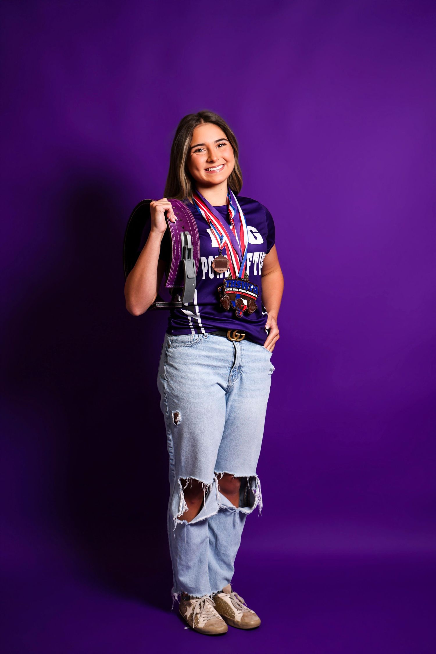 Athletic model in casual wear poses against purple backdrop during studio photoshoot.