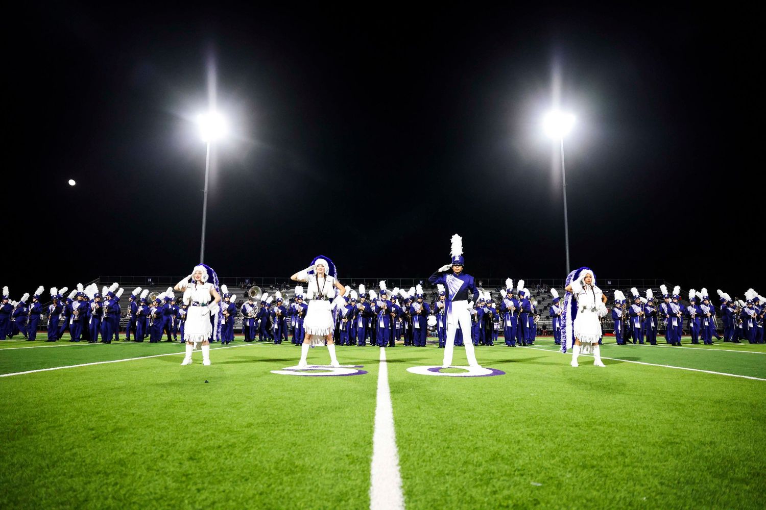 Stadium lights illuminating a football field at night with teams lined up.