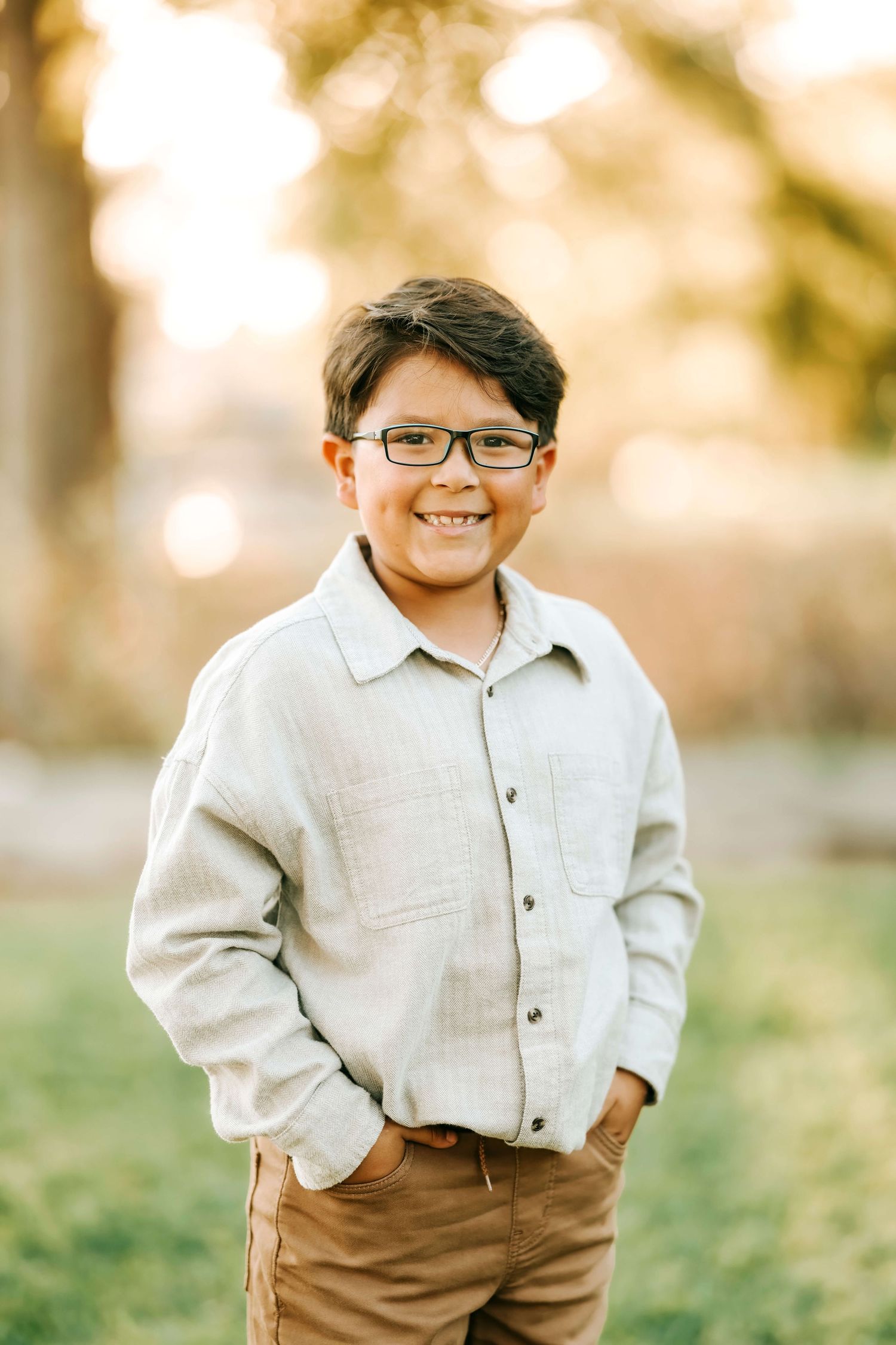 Young child in glasses wearing a light colored button-down shirt and brown pants outdoors.