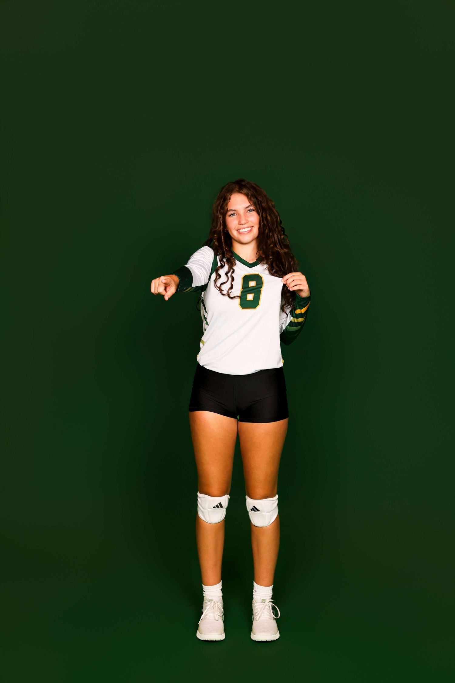 Volleyball player in white jersey poses against dark green background.