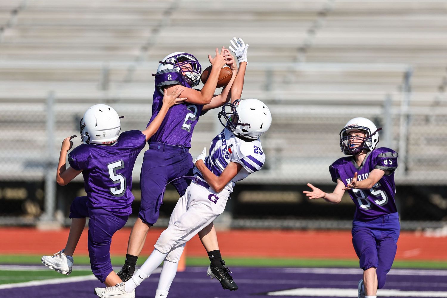 Football players in purple and white uniforms compete during intense game action.