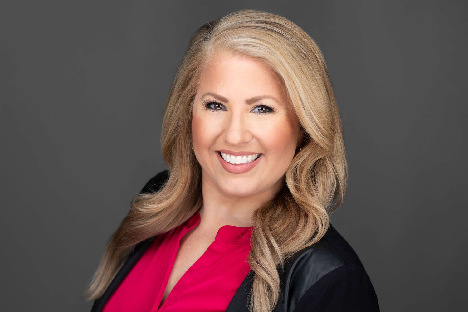 Professional studio portrait of person in black jacket and bright red top.