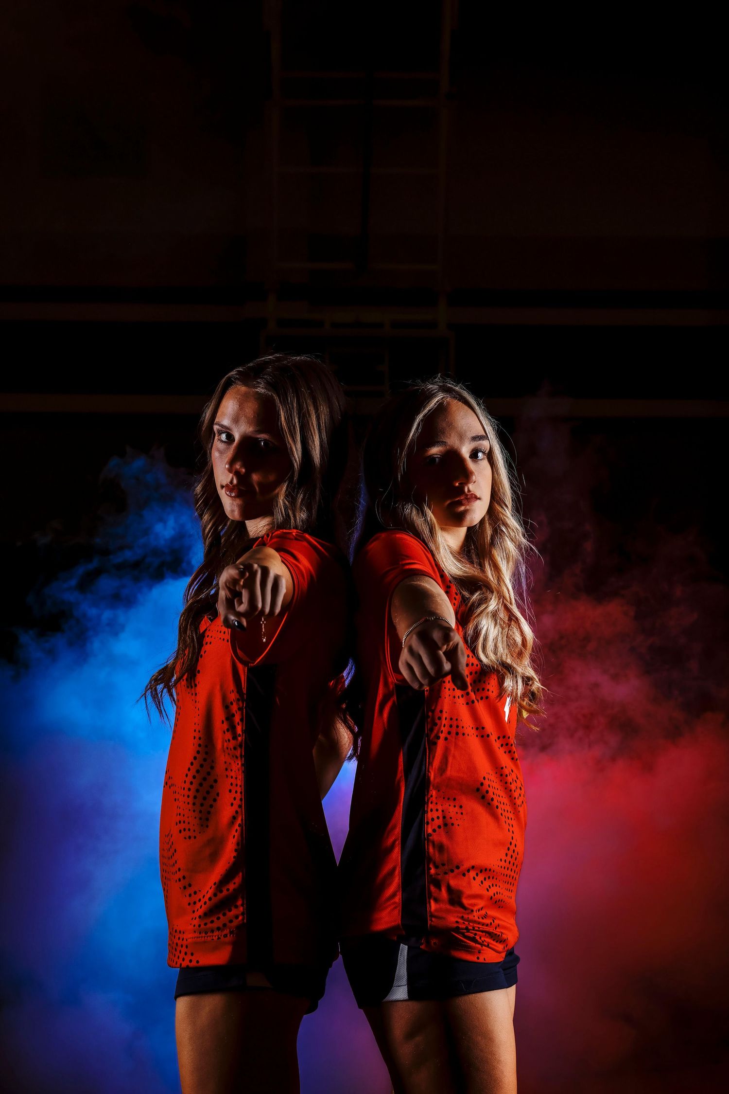 Two athletes in red uniforms pose back-to-back with dramatic smoke effects.