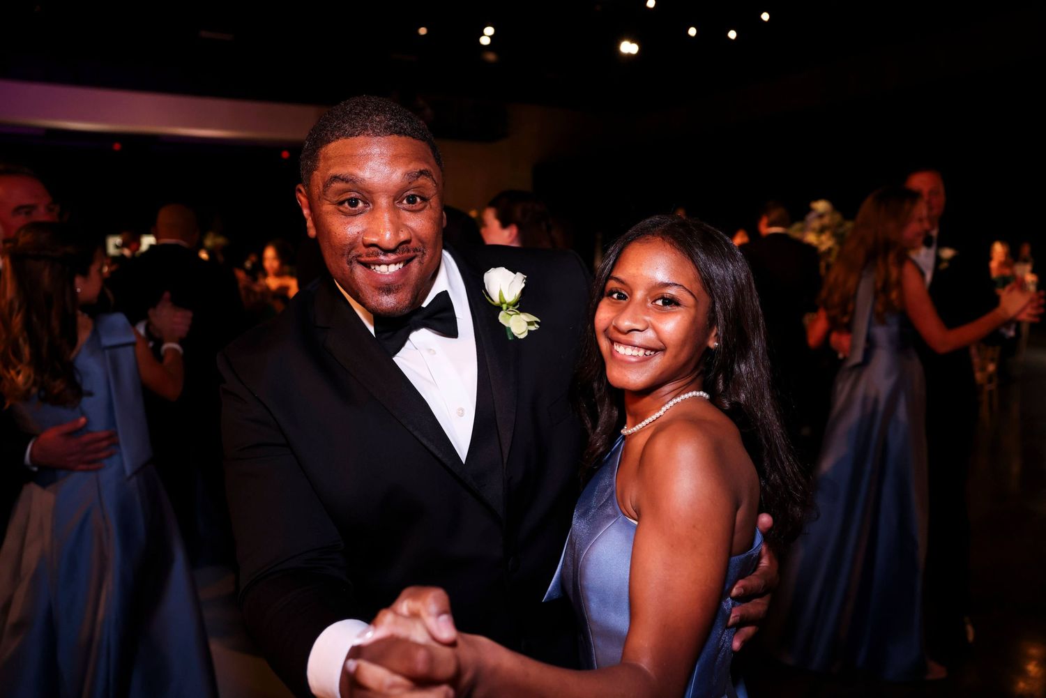 A group of people in formal attire smile and celebrate at an elegant evening event with dark lighting.