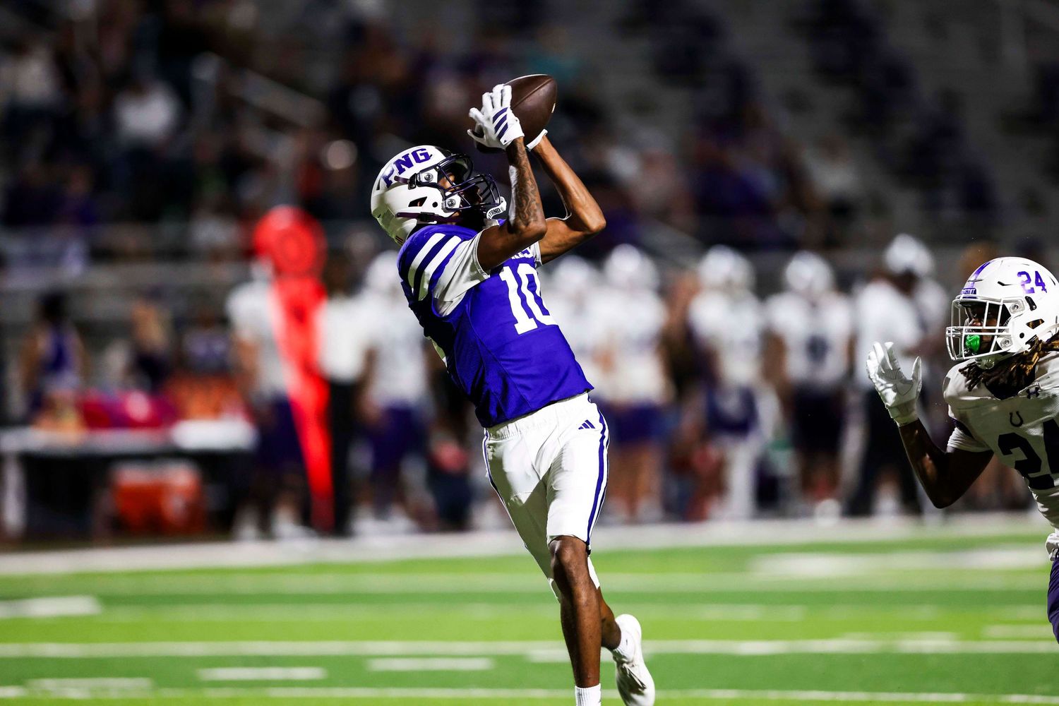 Wide receiver in purple jersey makes leaping catch during night game.