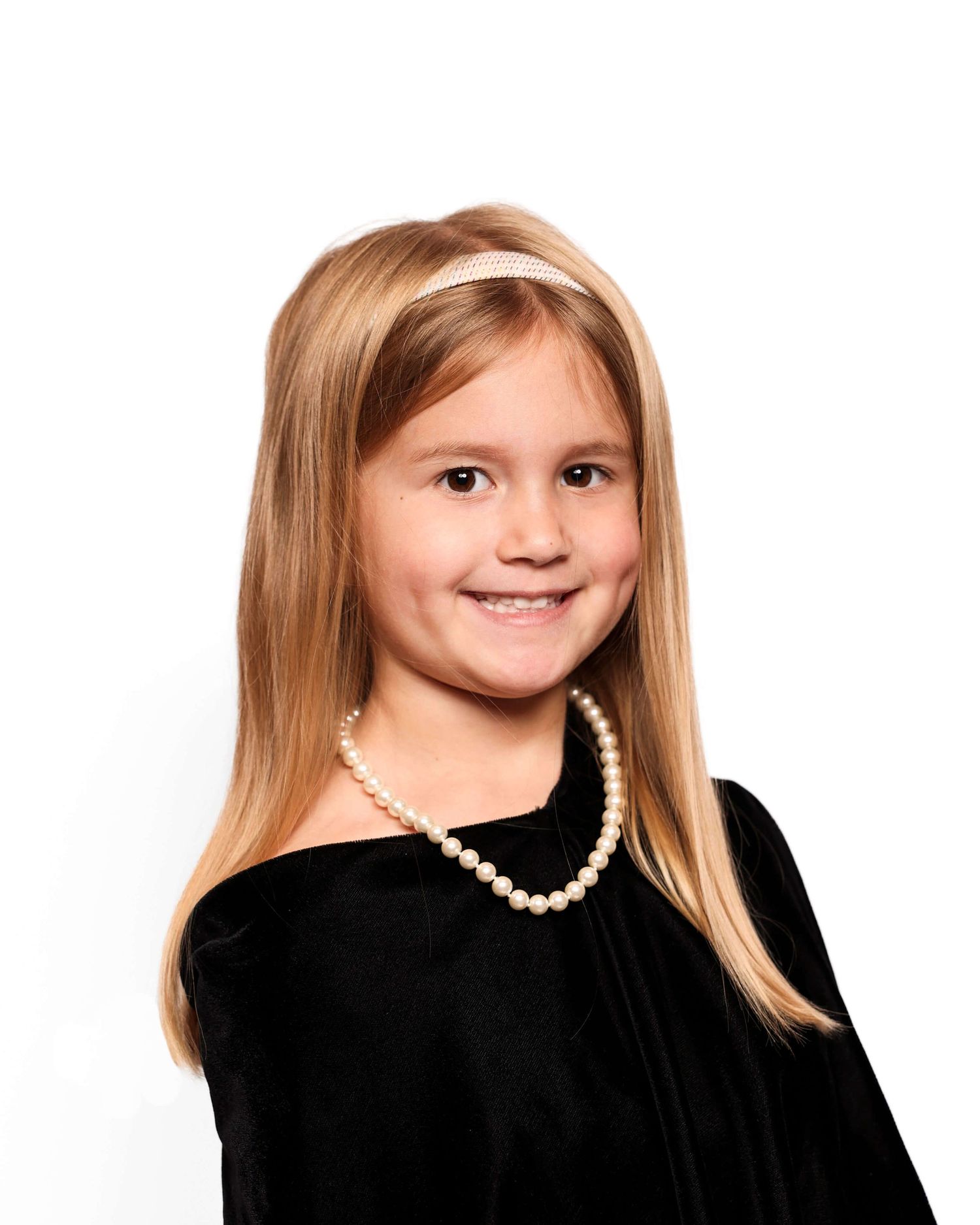 Four formal portraits of a child with straight blonde hair wearing a black dress and pearl necklace against white background.