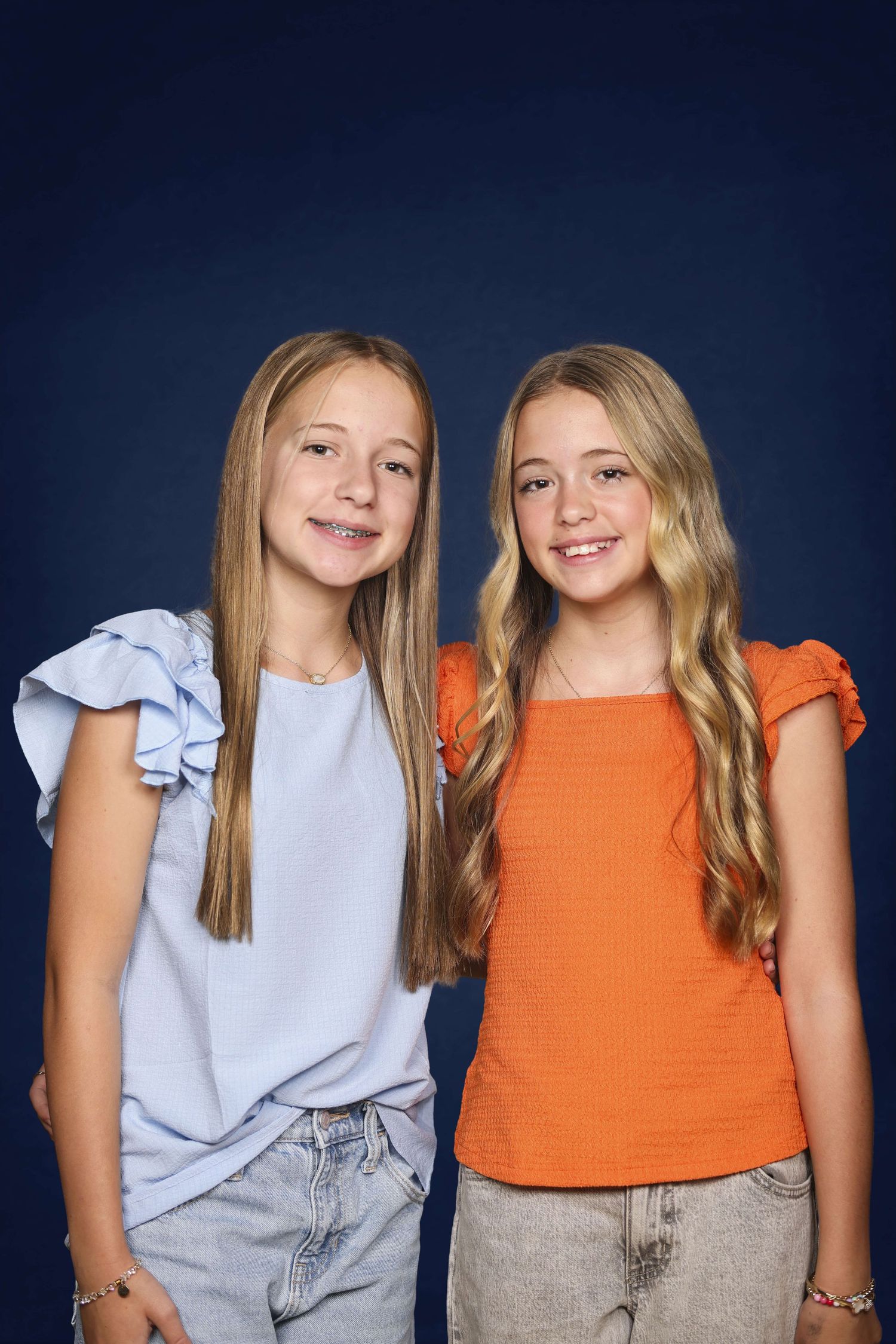 Two young friends wearing orange and blue tops pose together in a series of four similar photos against a dark background.