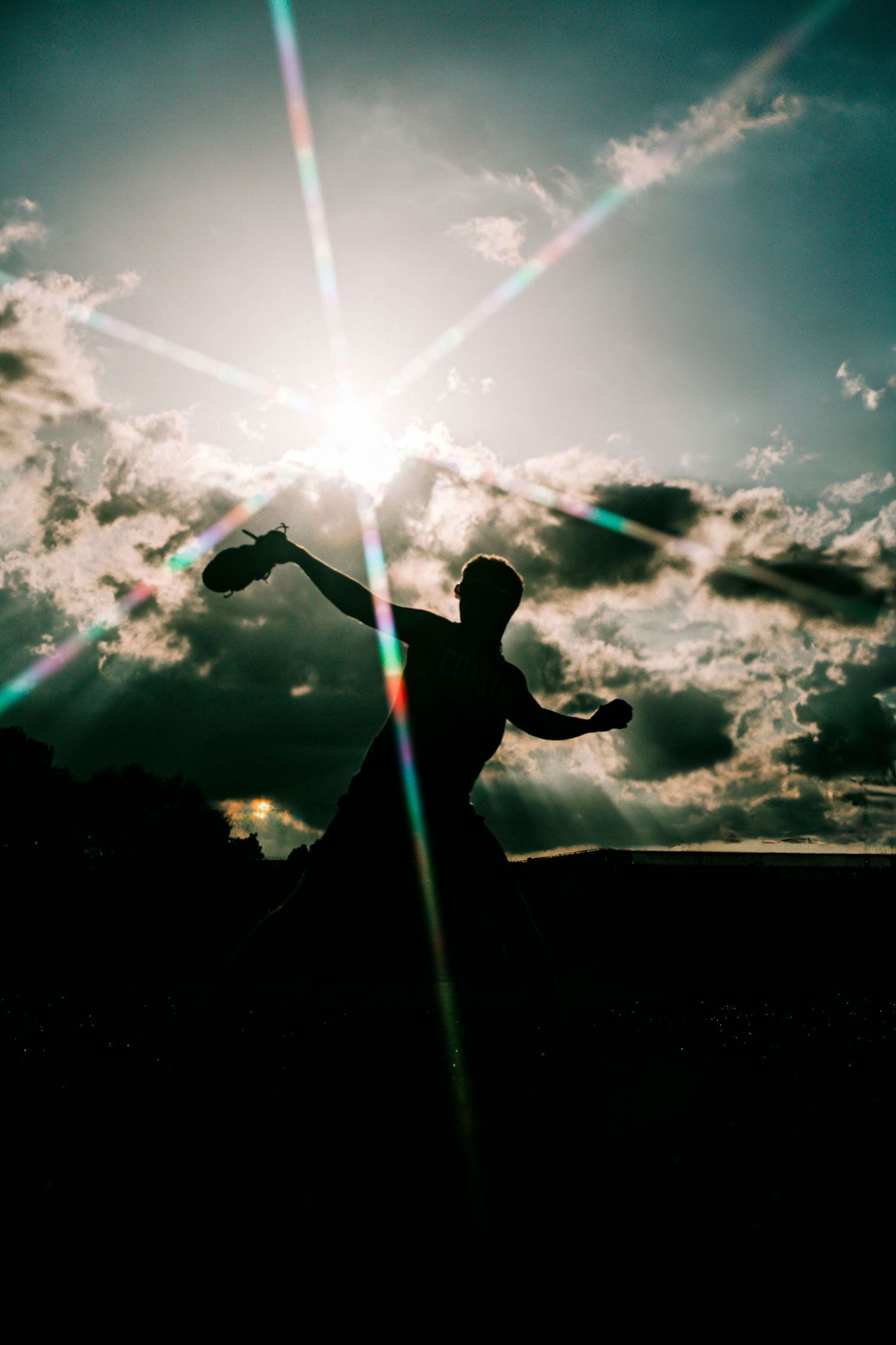 Dramatic silhouette of baseball players against sunset sky with lens flare.