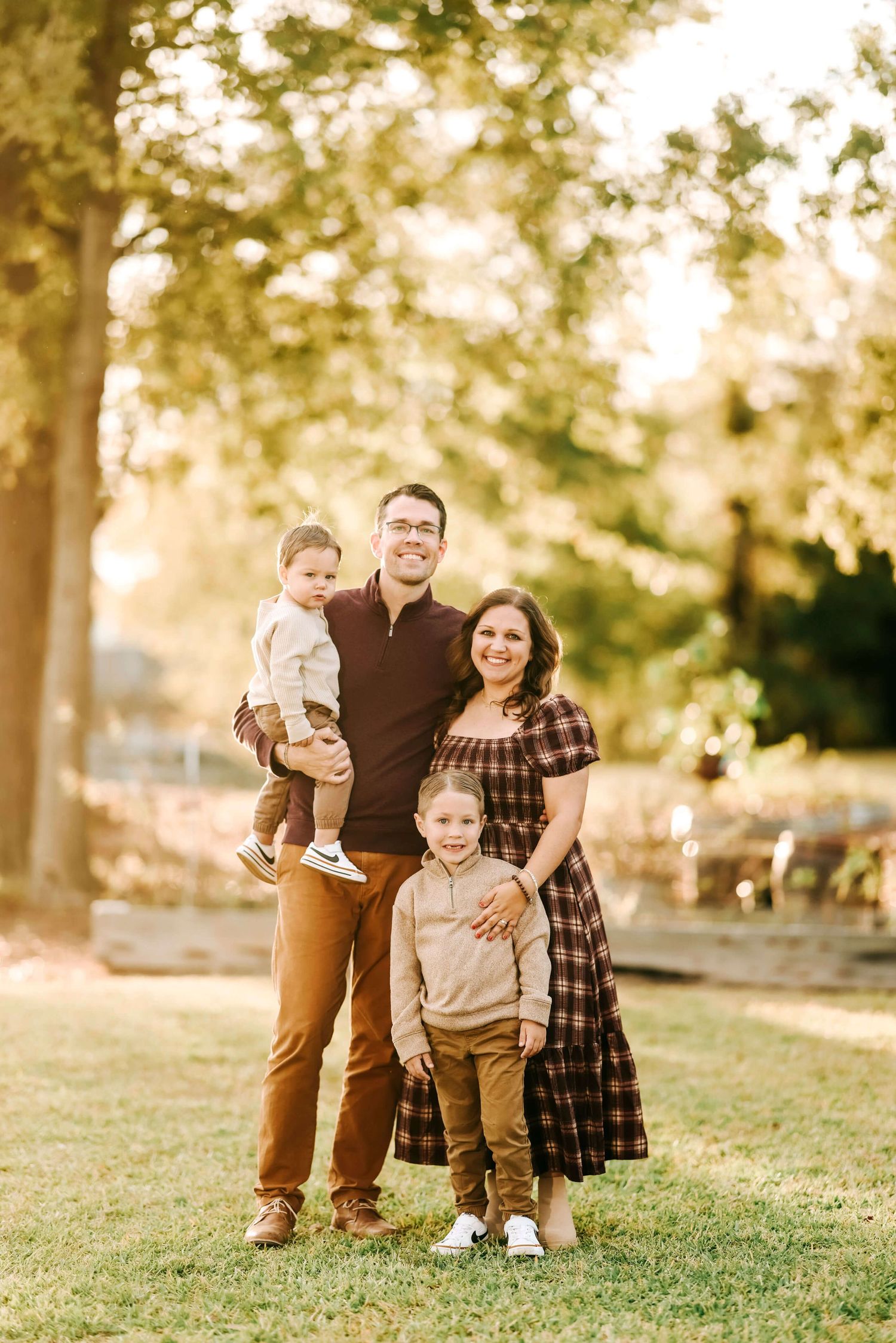 Family portrait in autumn setting with warm golden sunlight filtering through trees.