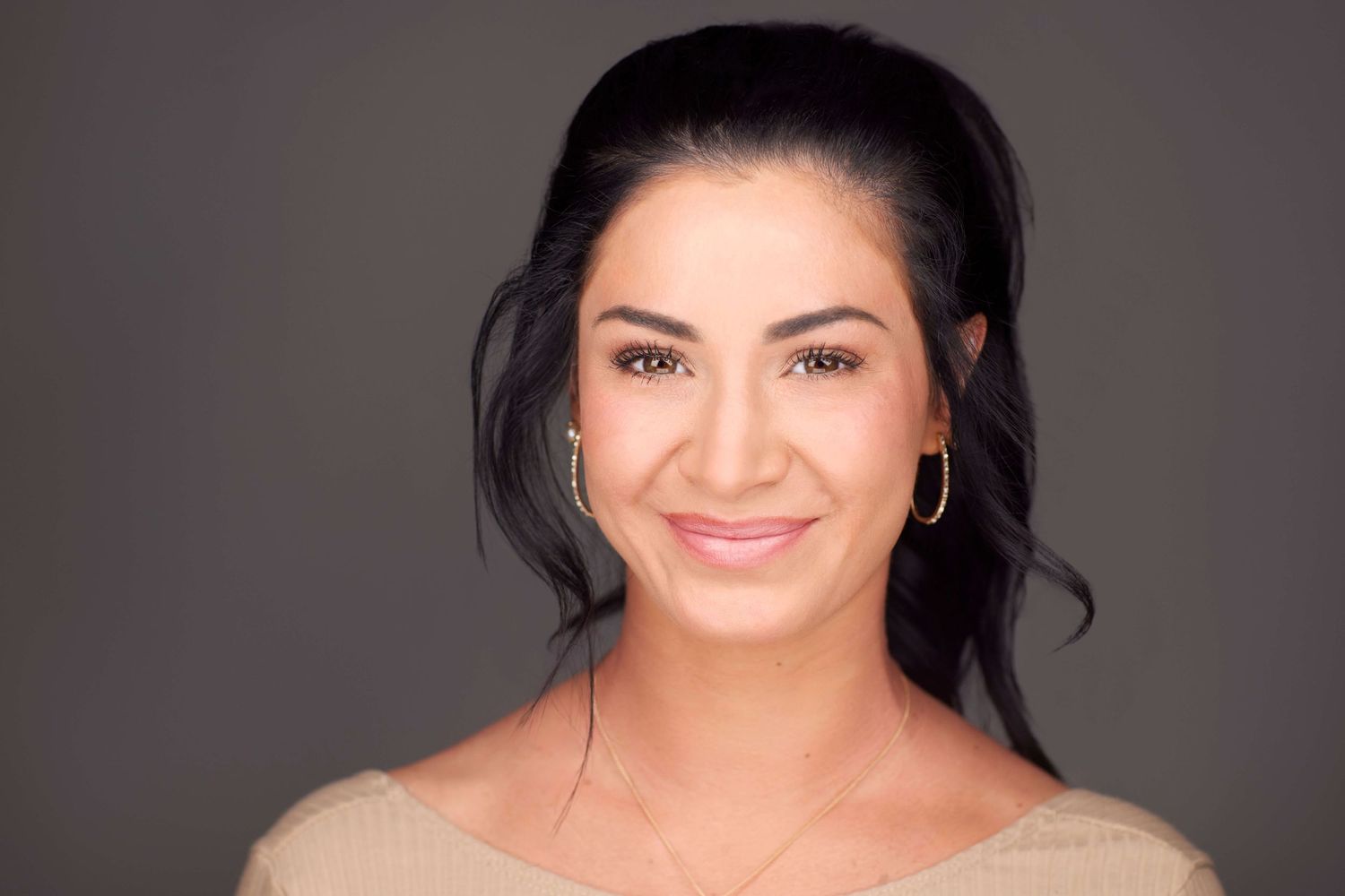 Professional headshot of person smiling warmly against dark studio backdrop.