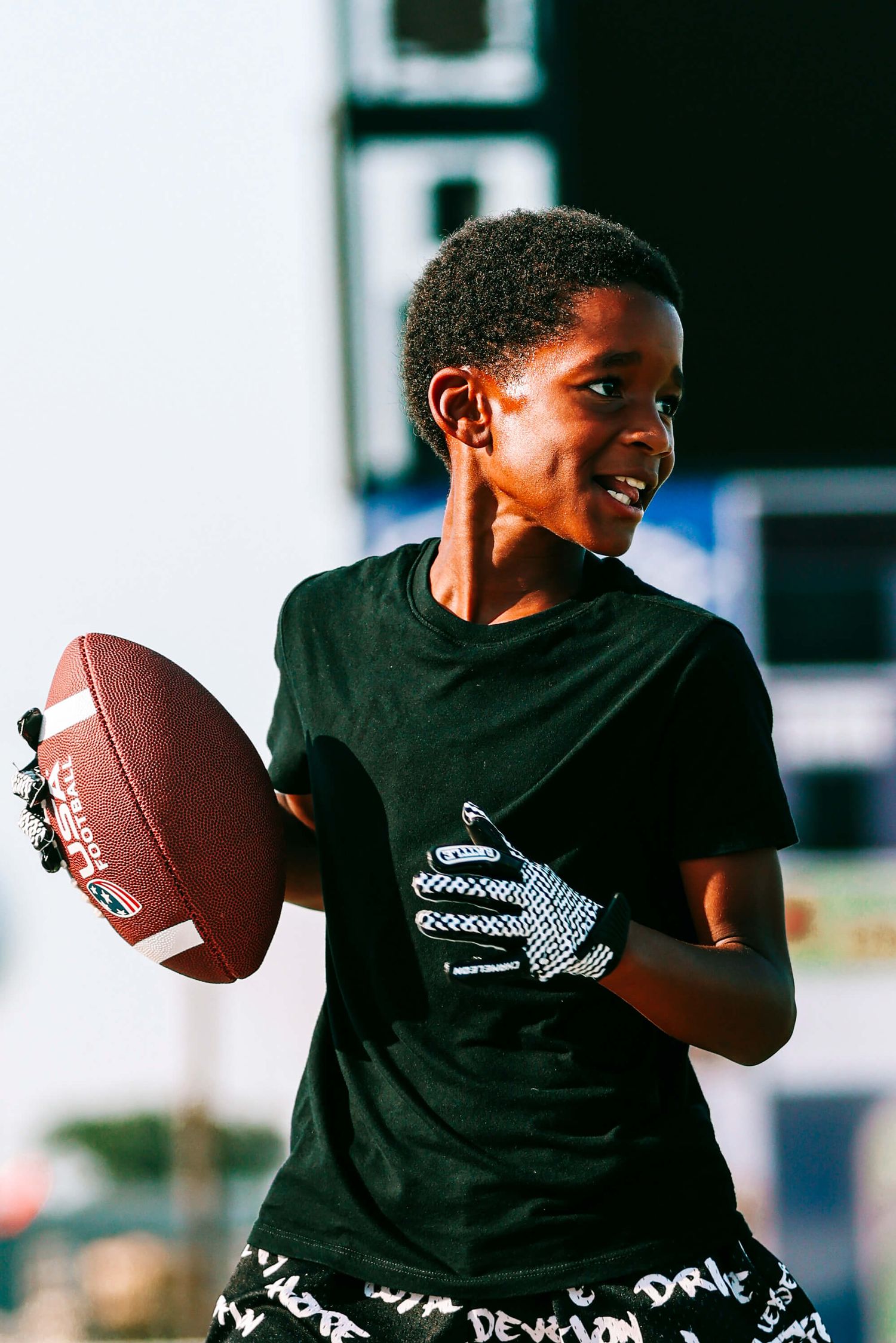 Young athlete in black t-shirt practices throwing a football in sequential motion.