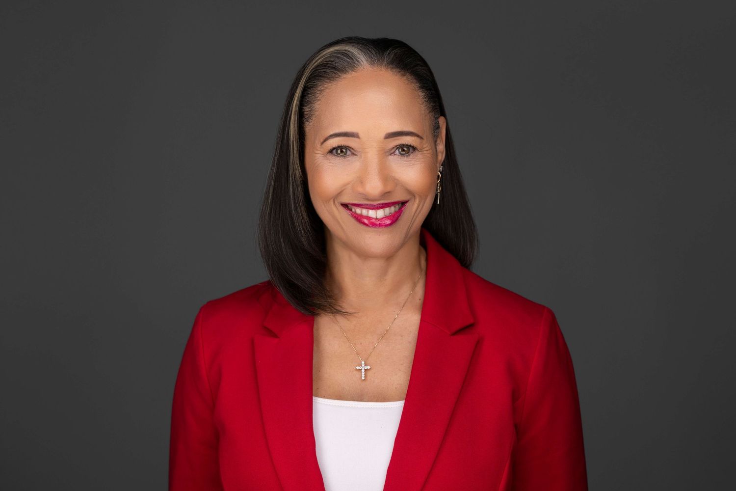 Professional headshot of someone wearing red blazer with white top against dark background.