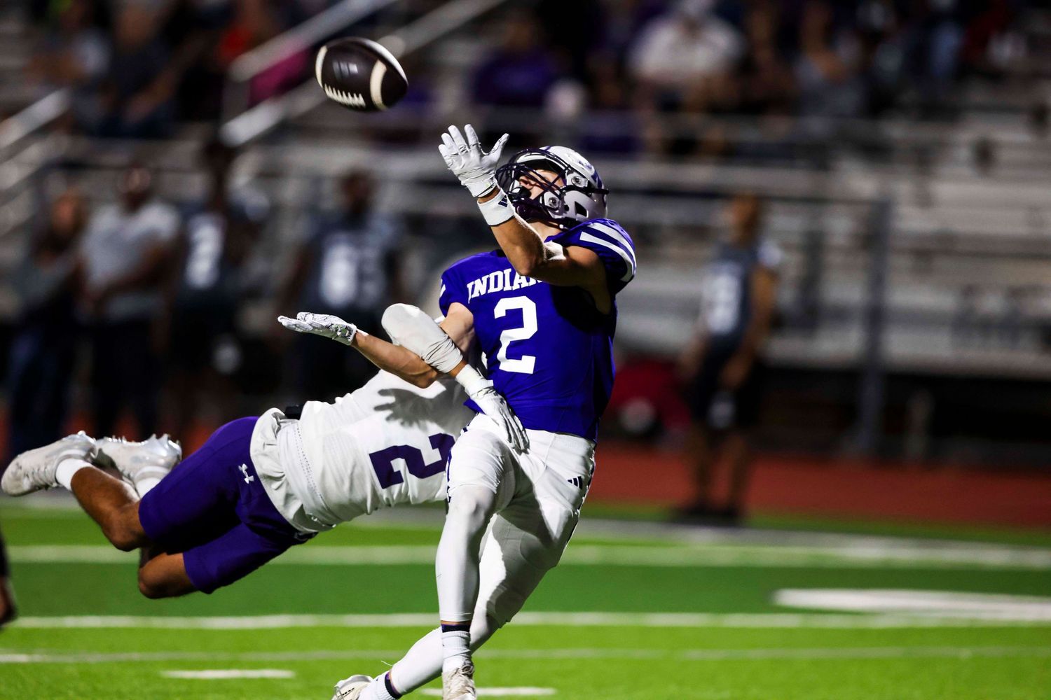 Football player leaping to catch pass while defender attempts to block.