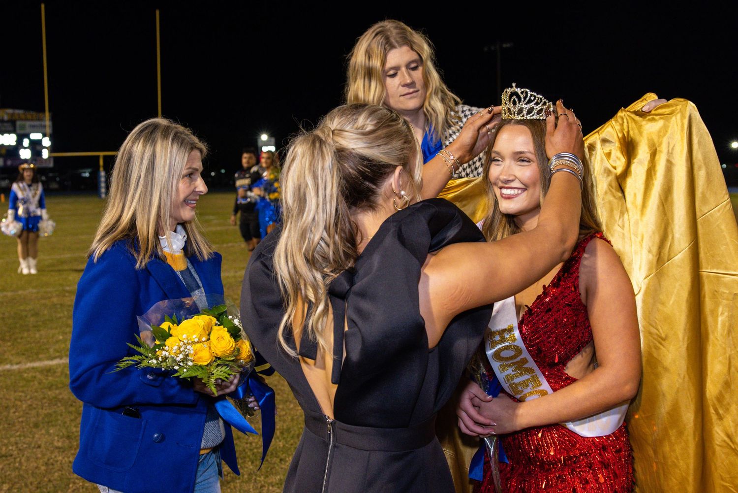 Students celebrate at a formal event wearing gowns and crowns during a special ceremony.