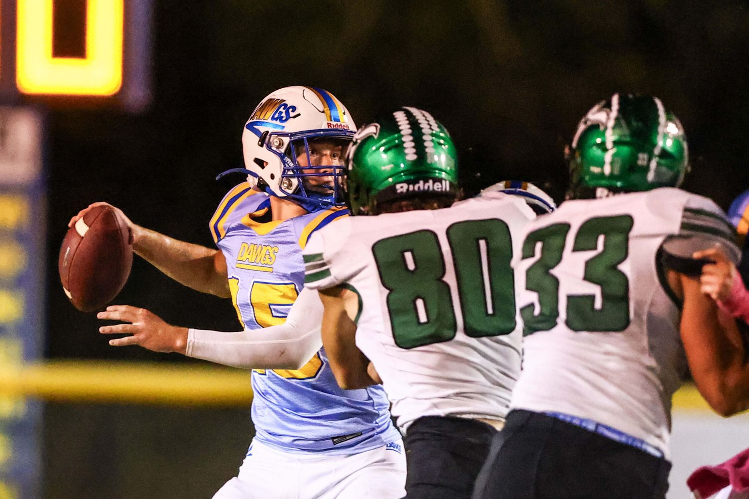 Football players from opposing teams clash during nighttime game under stadium lights.