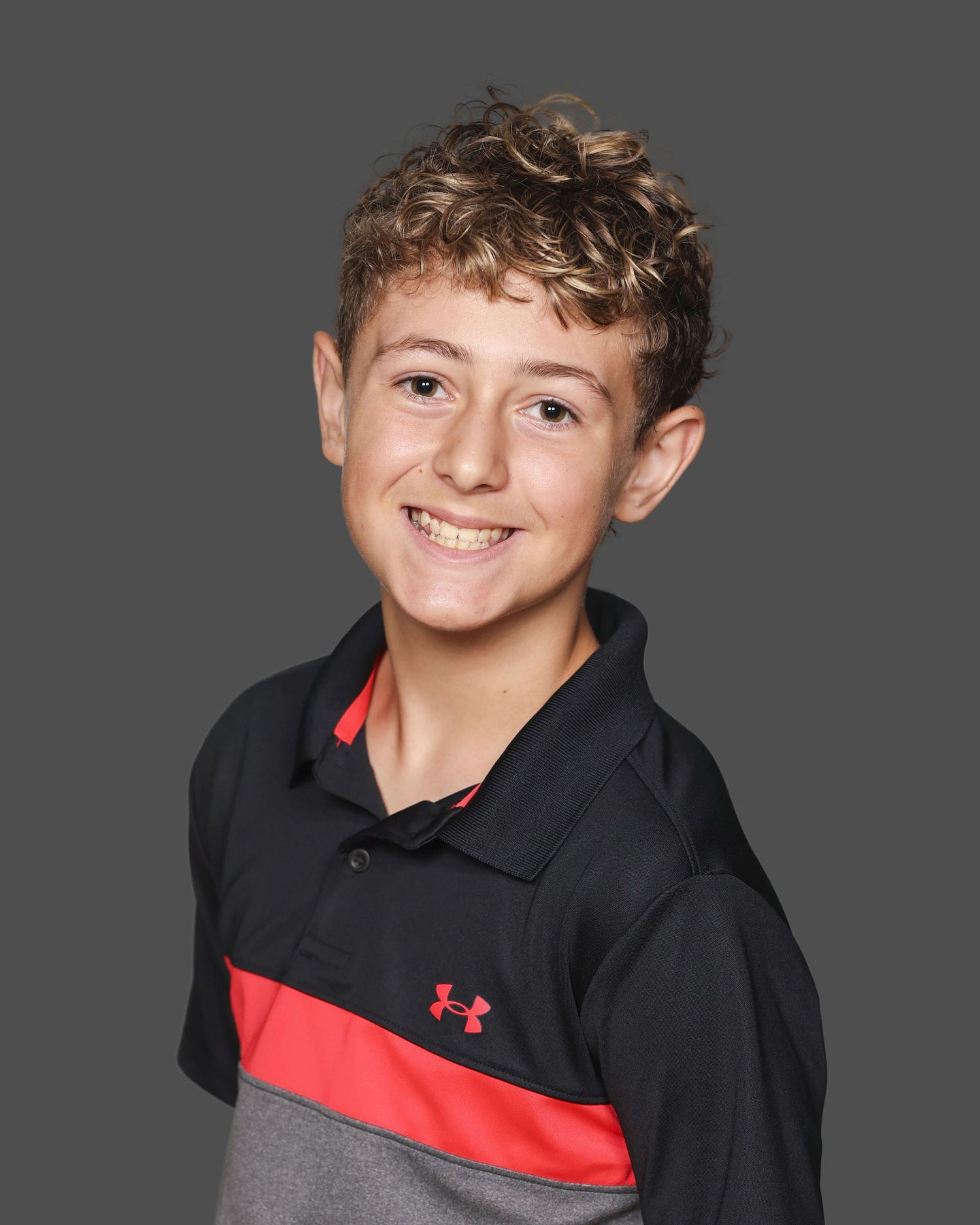 Young person in black and red athletic wear smiling at camera against gray background.