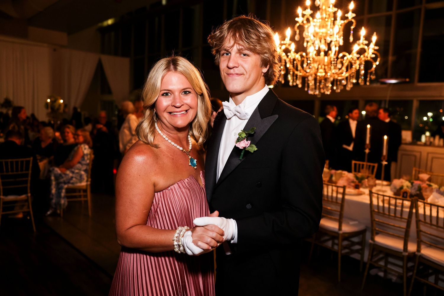 A couple poses together at an elegant wedding reception with a crystal chandelier overhead in a formal venue.