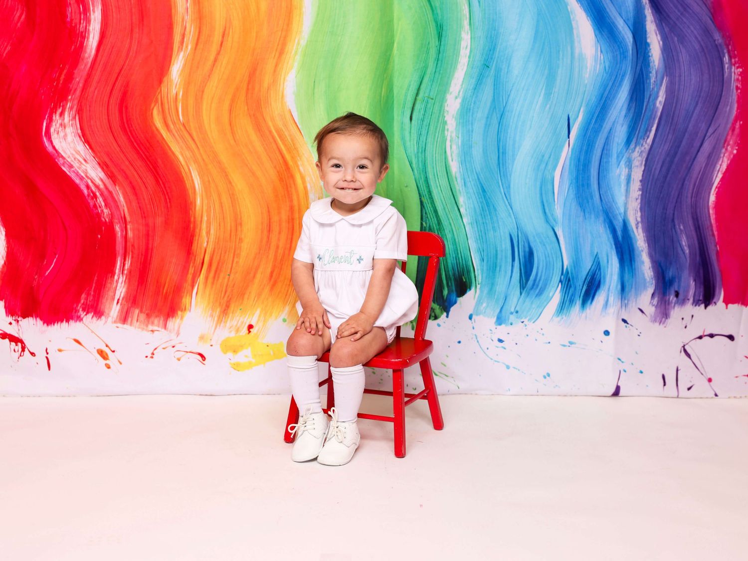 Rainbow watercolor wall serves as vibrant backdrop for child photography session.