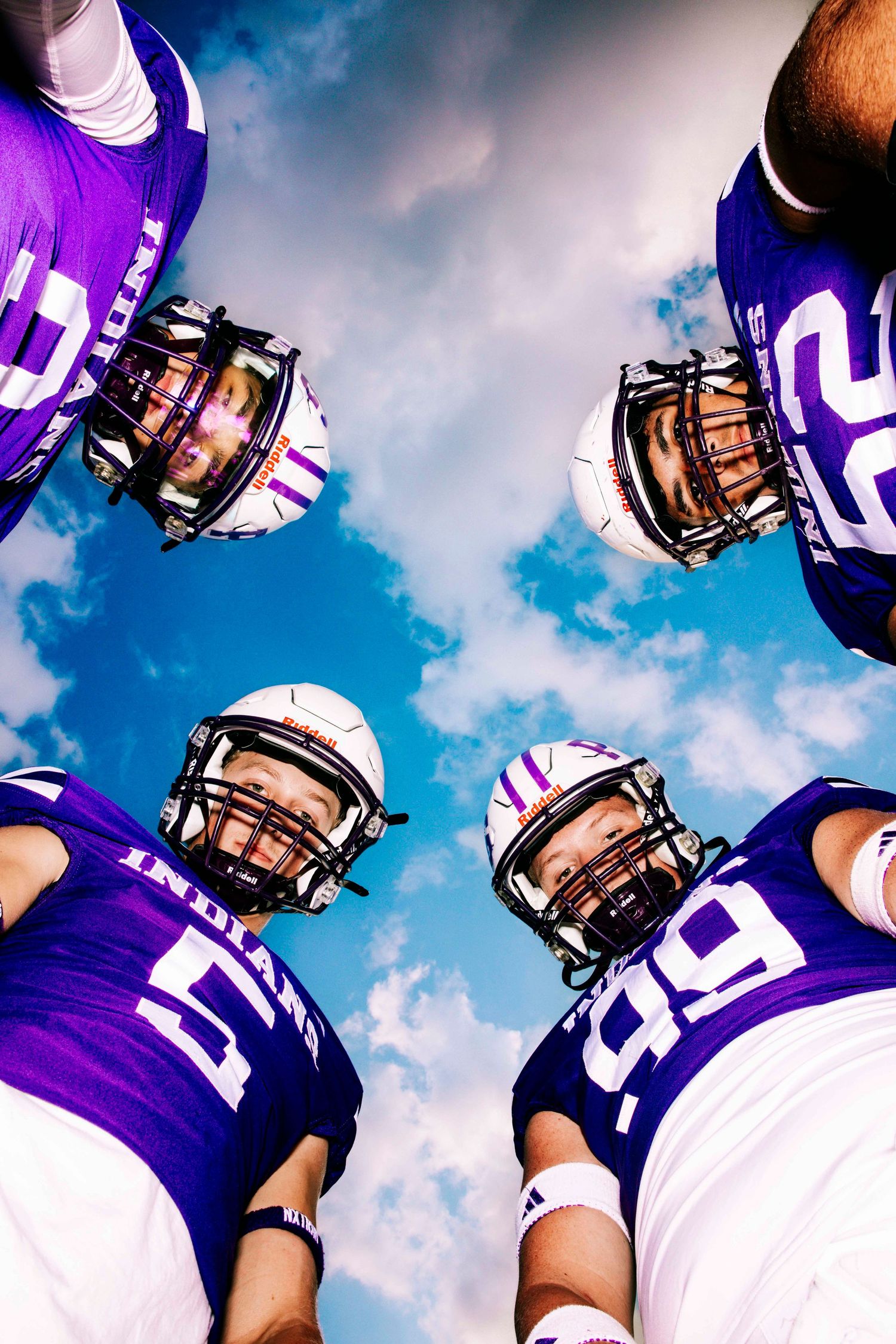Football team members in purple jerseys looking up against blue sky with clouds.