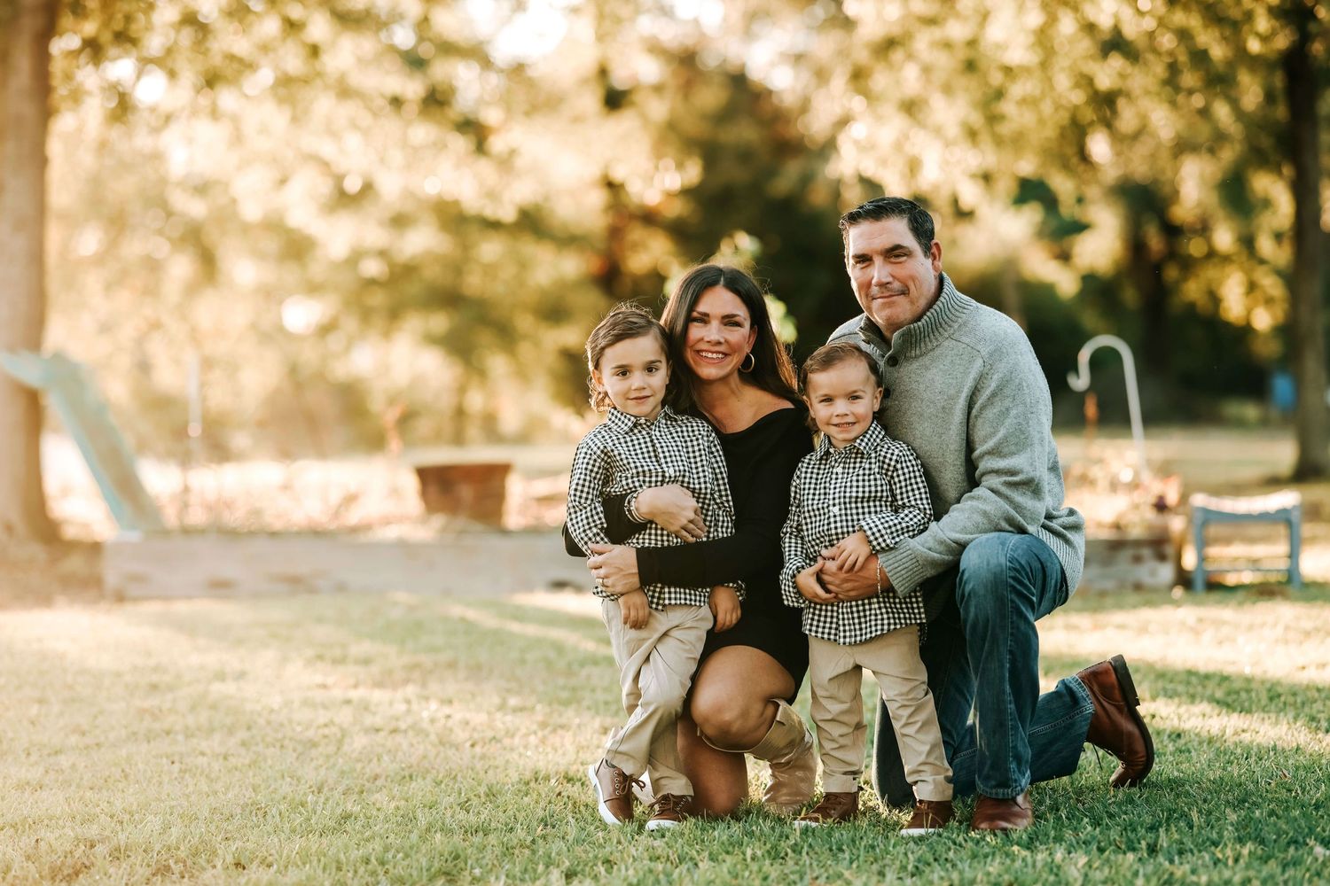 Casual family portrait session with everyone kneeling together on grass during golden hour.