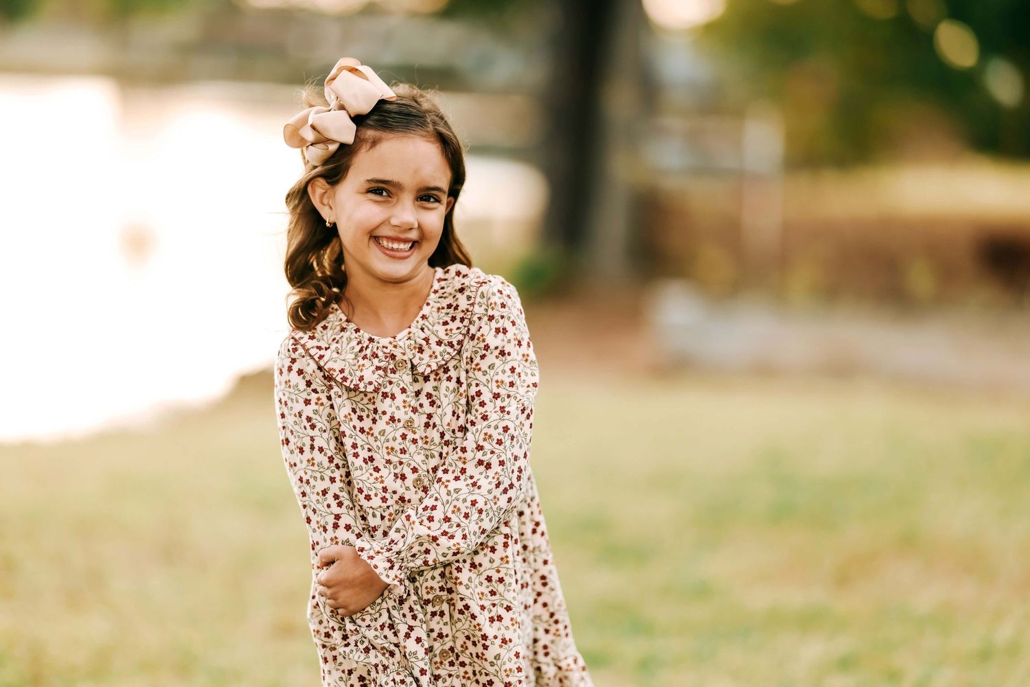 Young person in a floral print dress posing outdoors during golden hour.