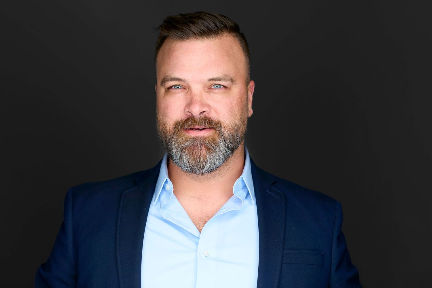 Business portrait of person in navy suit and light blue shirt against dark background.