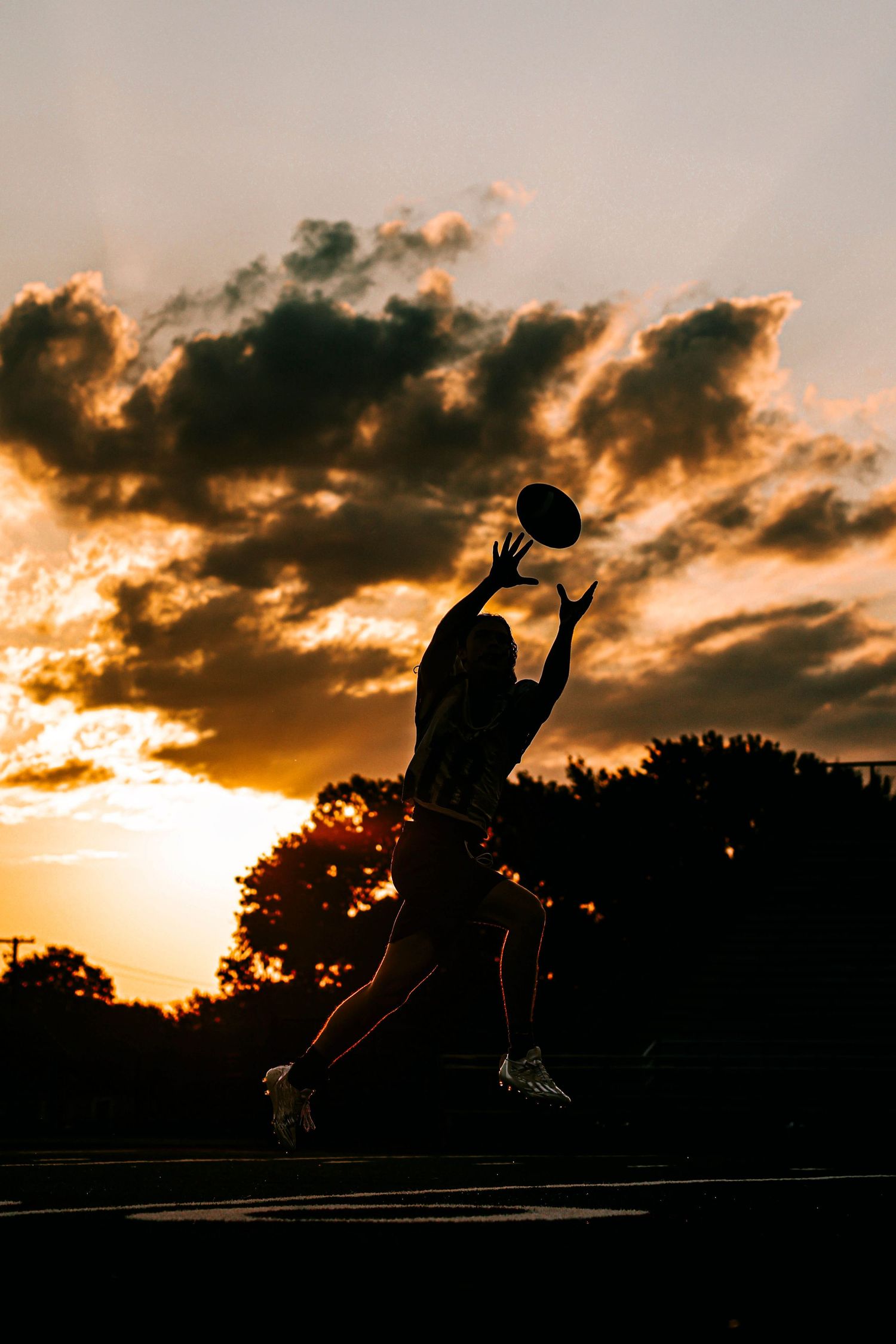Silhouette of football player catching ball against dramatic sunset sky.