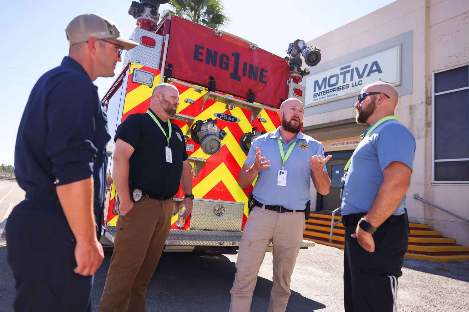 Group of firefighters and emergency responders gathered outside a building with fire engine visible.