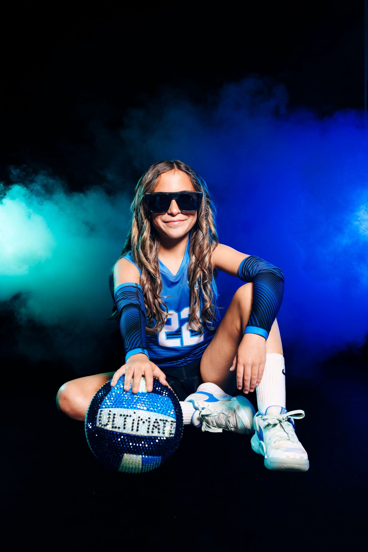 Volleyball player in blue jersey poses with ball amid colorful smoke effects.