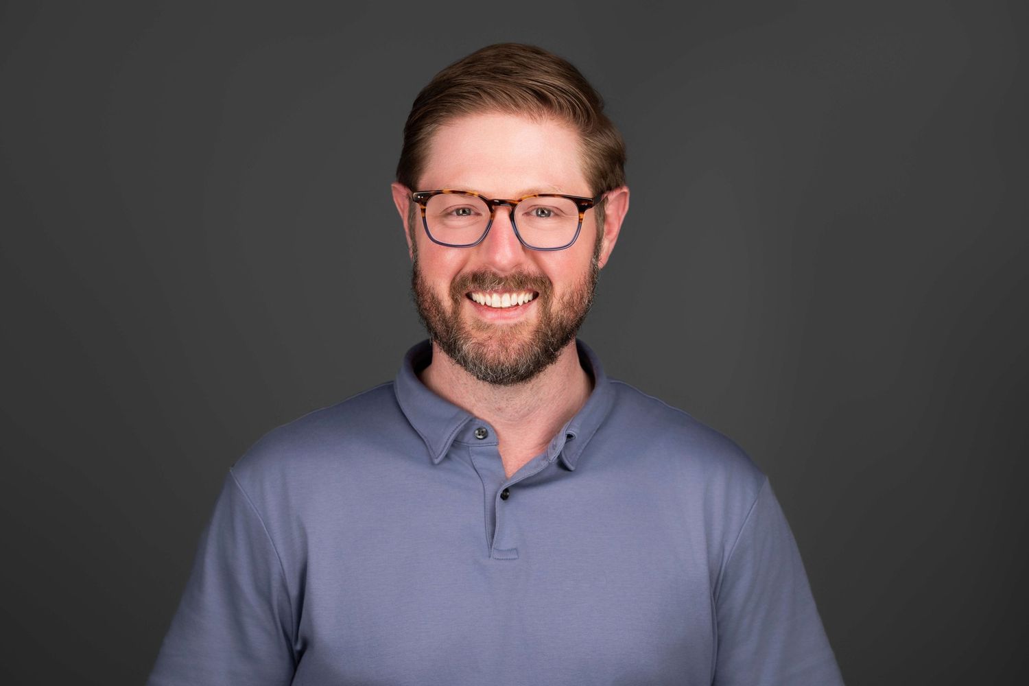 Professional headshot of person in business attire smiling against dark background.