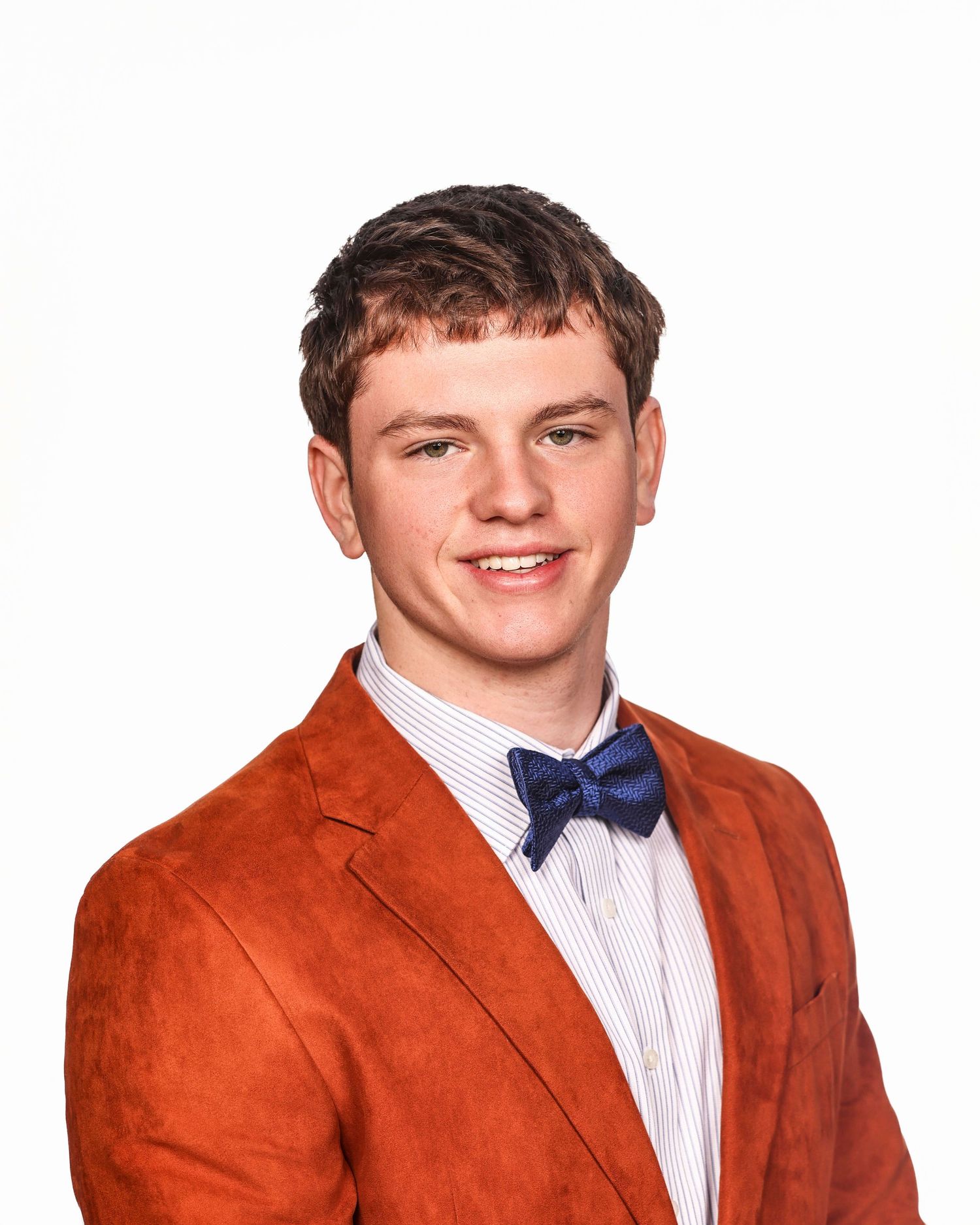 A person wearing a bright orange blazer and navy bow tie smiles while posing against a white background.