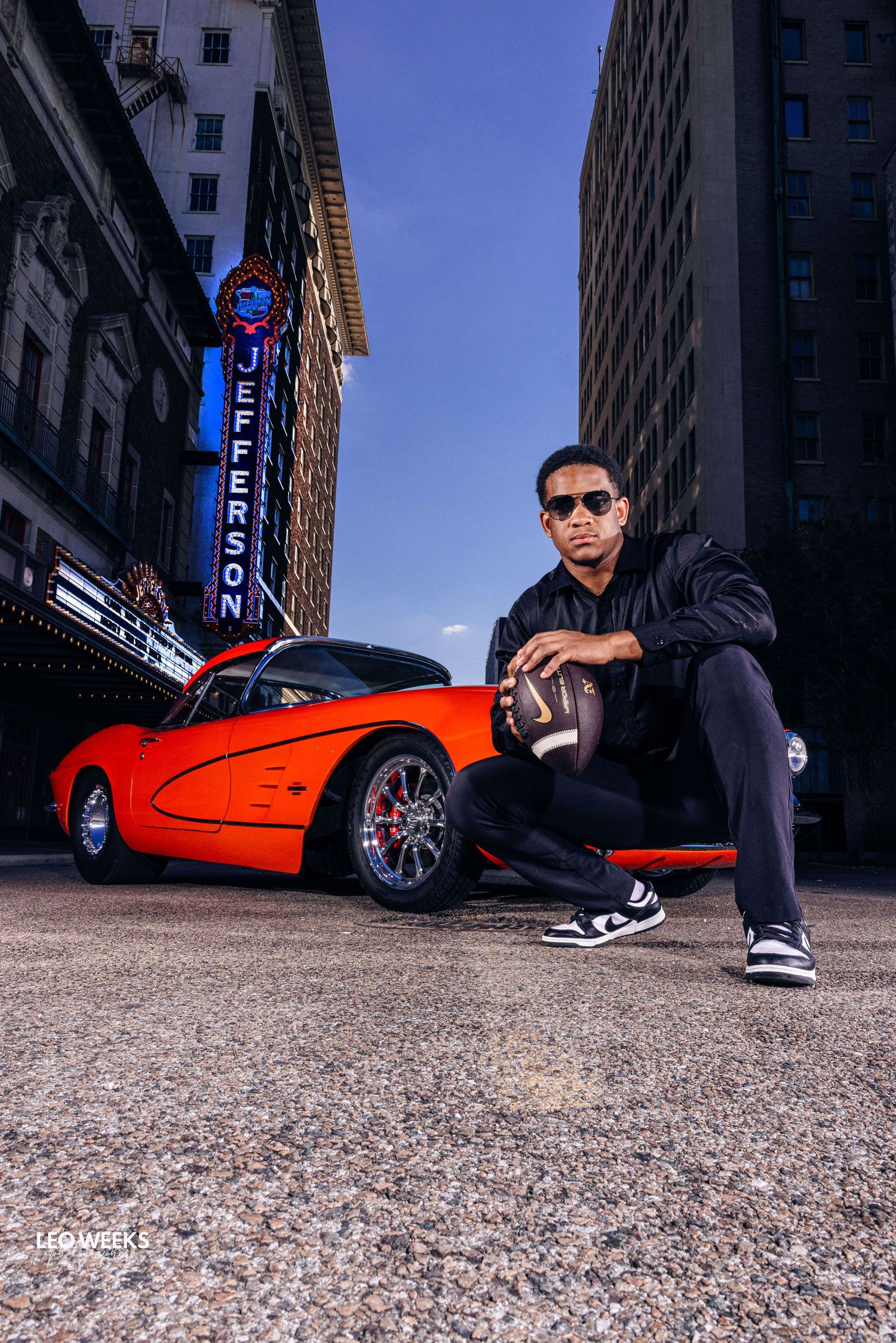 Urban photoshoot featuring red sports car and person in casual attire on city street.