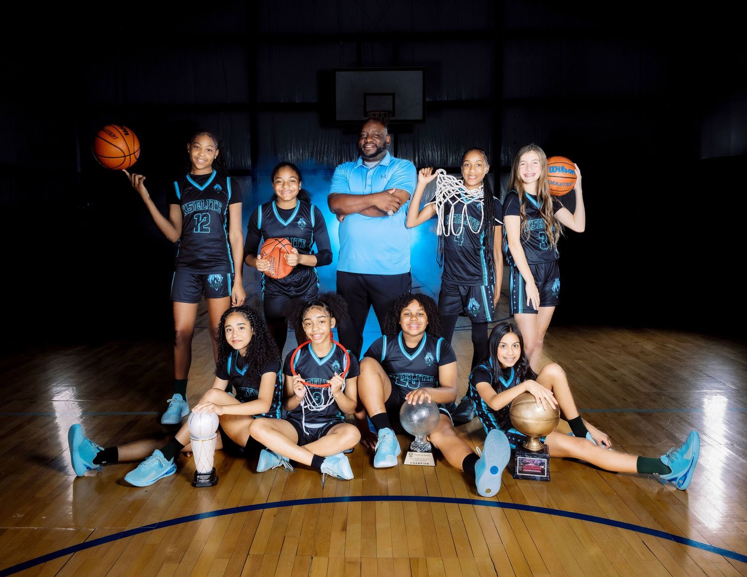 Basketball team and coach pose together on indoor court with balls.