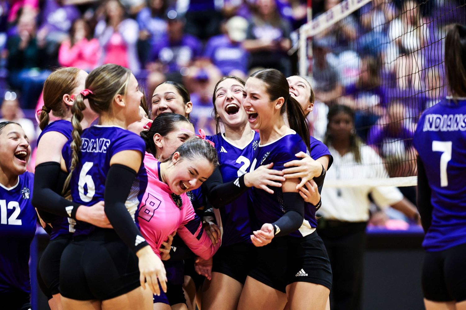 Volleyball team in purple uniforms celebrating a point with excitement.