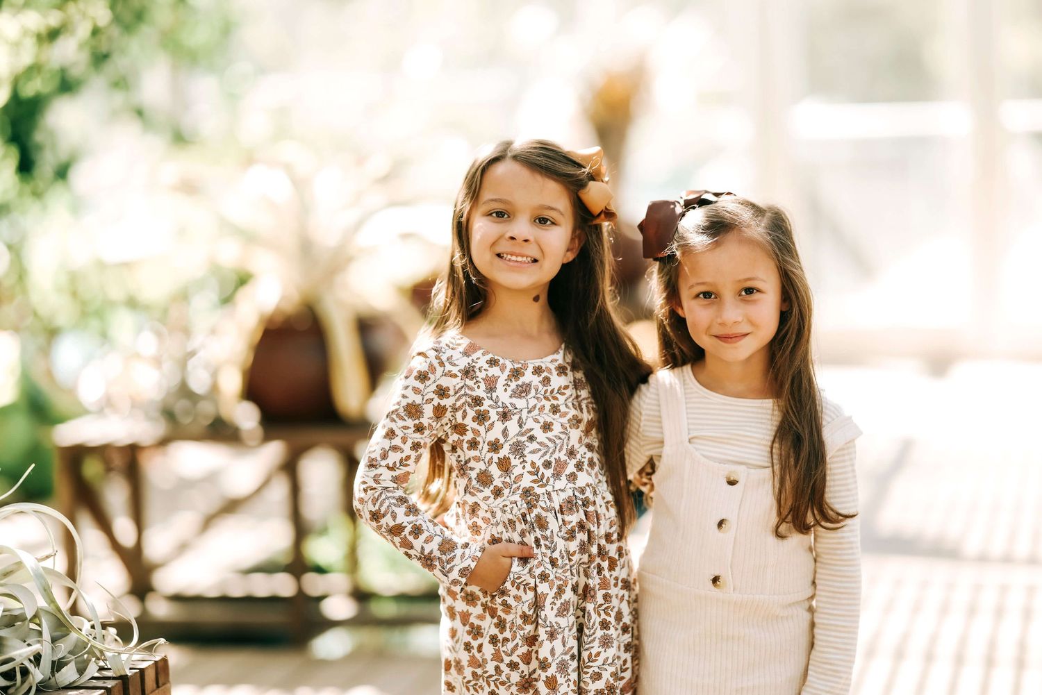 Two young girls standing together, one wearing a floral dress and one in a white outfit.