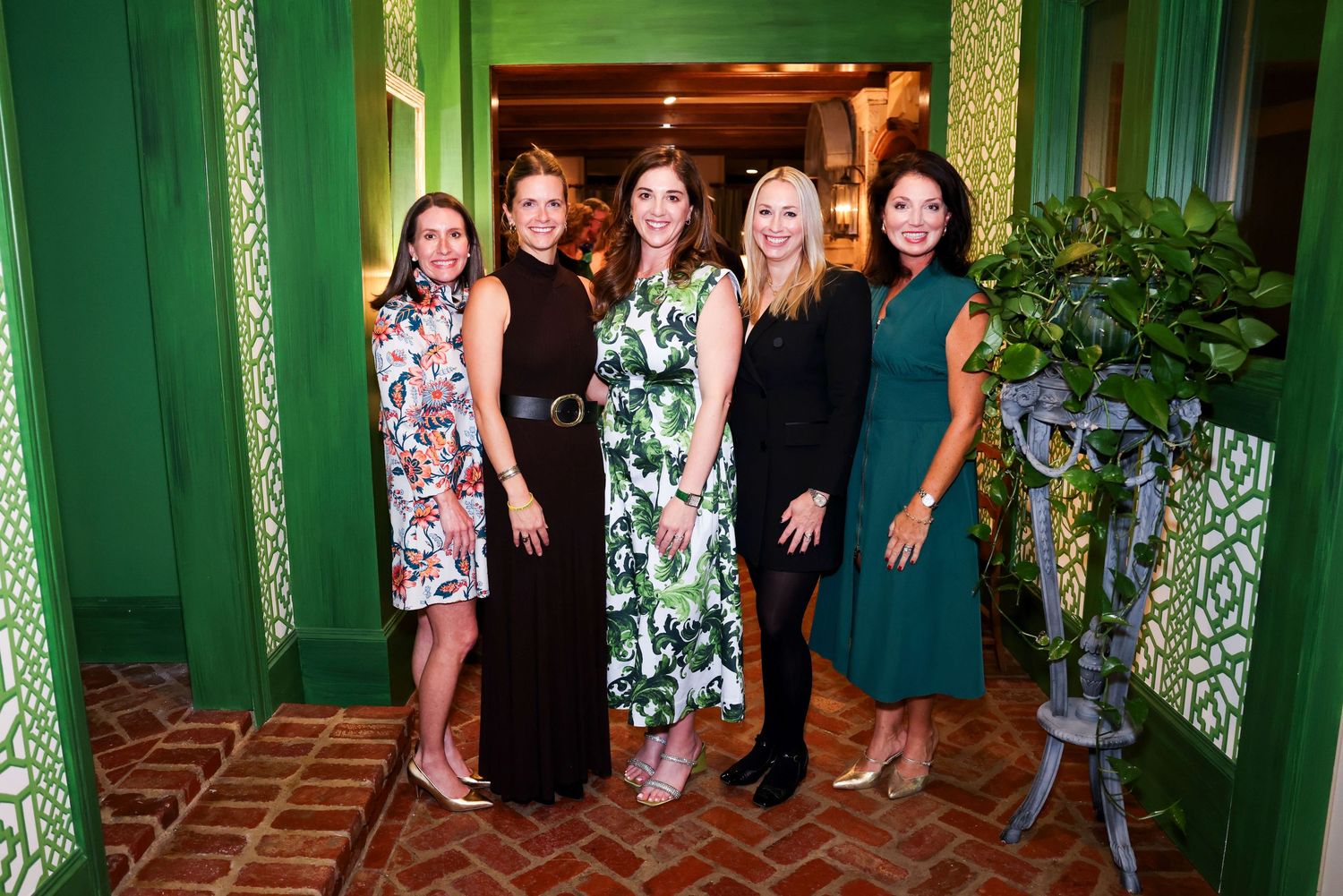 A group of people stand in a row against a green wall at a formal event.