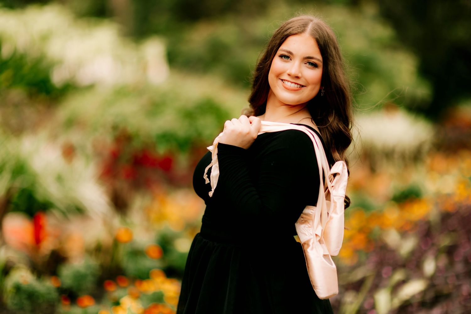 Woman in black dress poses outdoors in autumn garden with vibrant flowers and natural lighting.